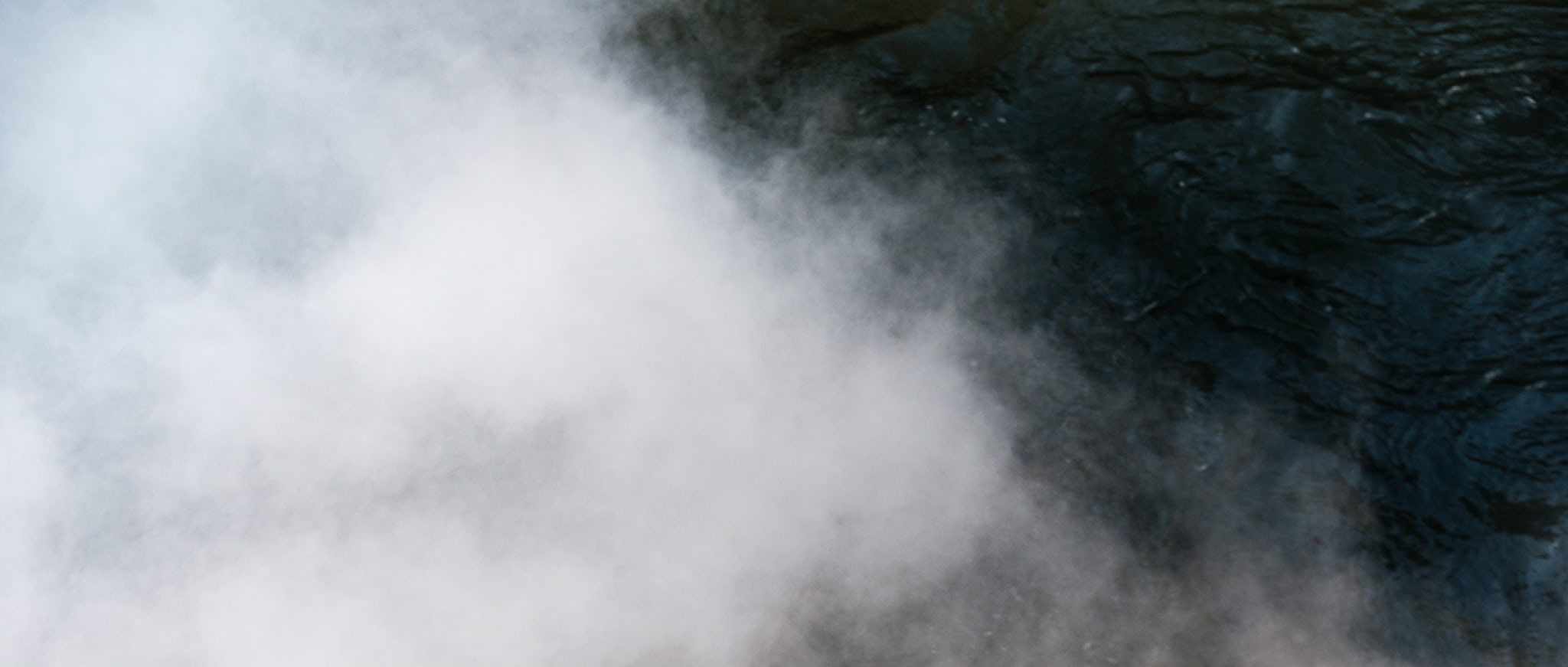 Waterfall mist rising next to dark flowing water.