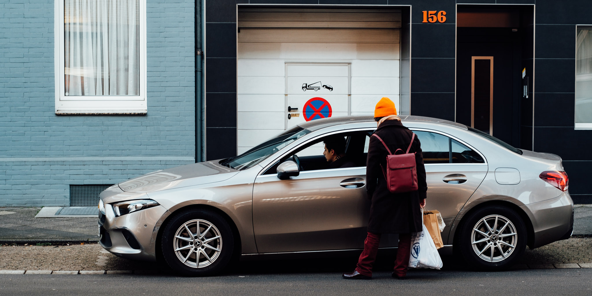 A woman with shopping bags gets into a modern silver car parked on a city street.