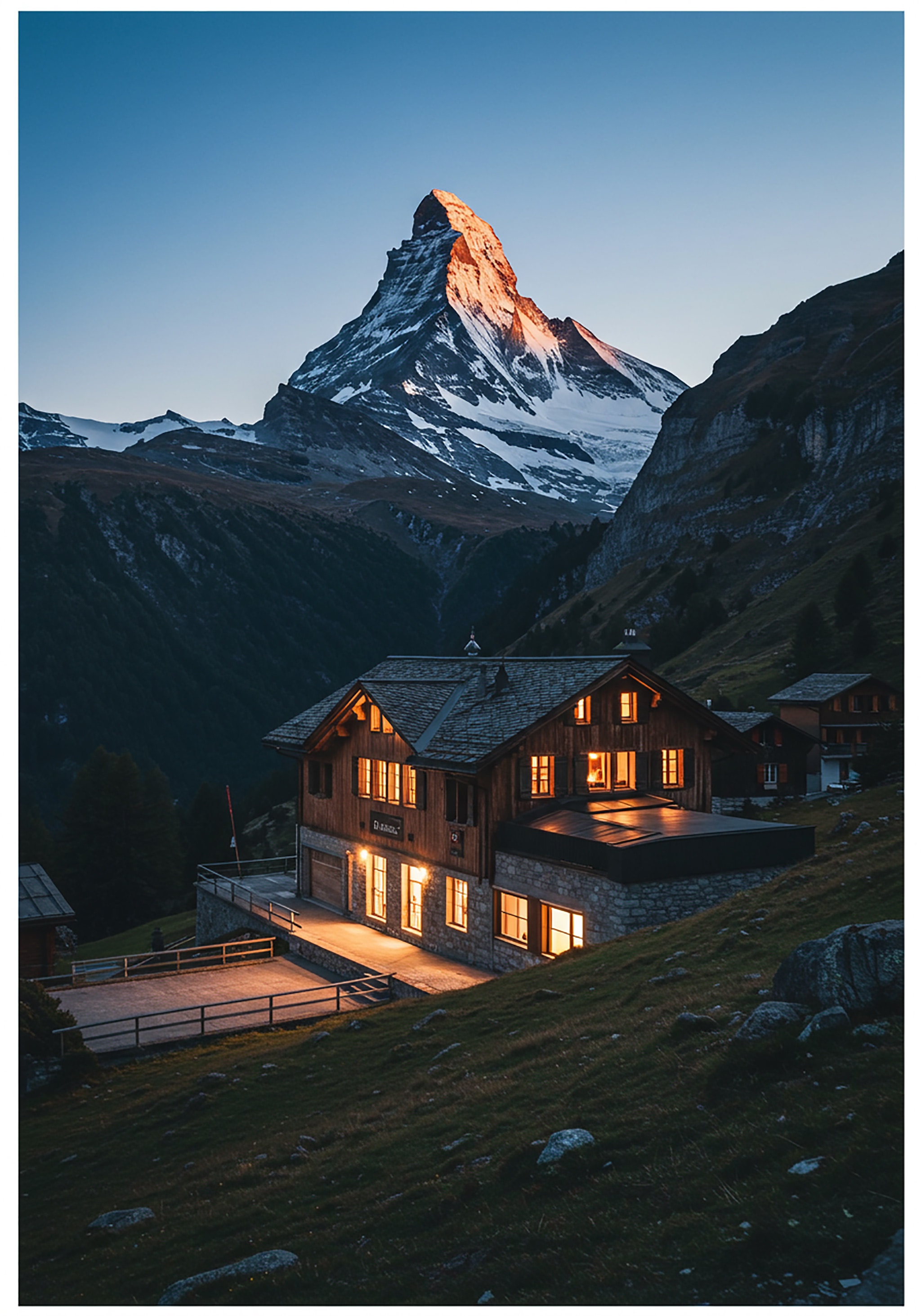 Cabin with illuminated windows below a mountain at sunset.