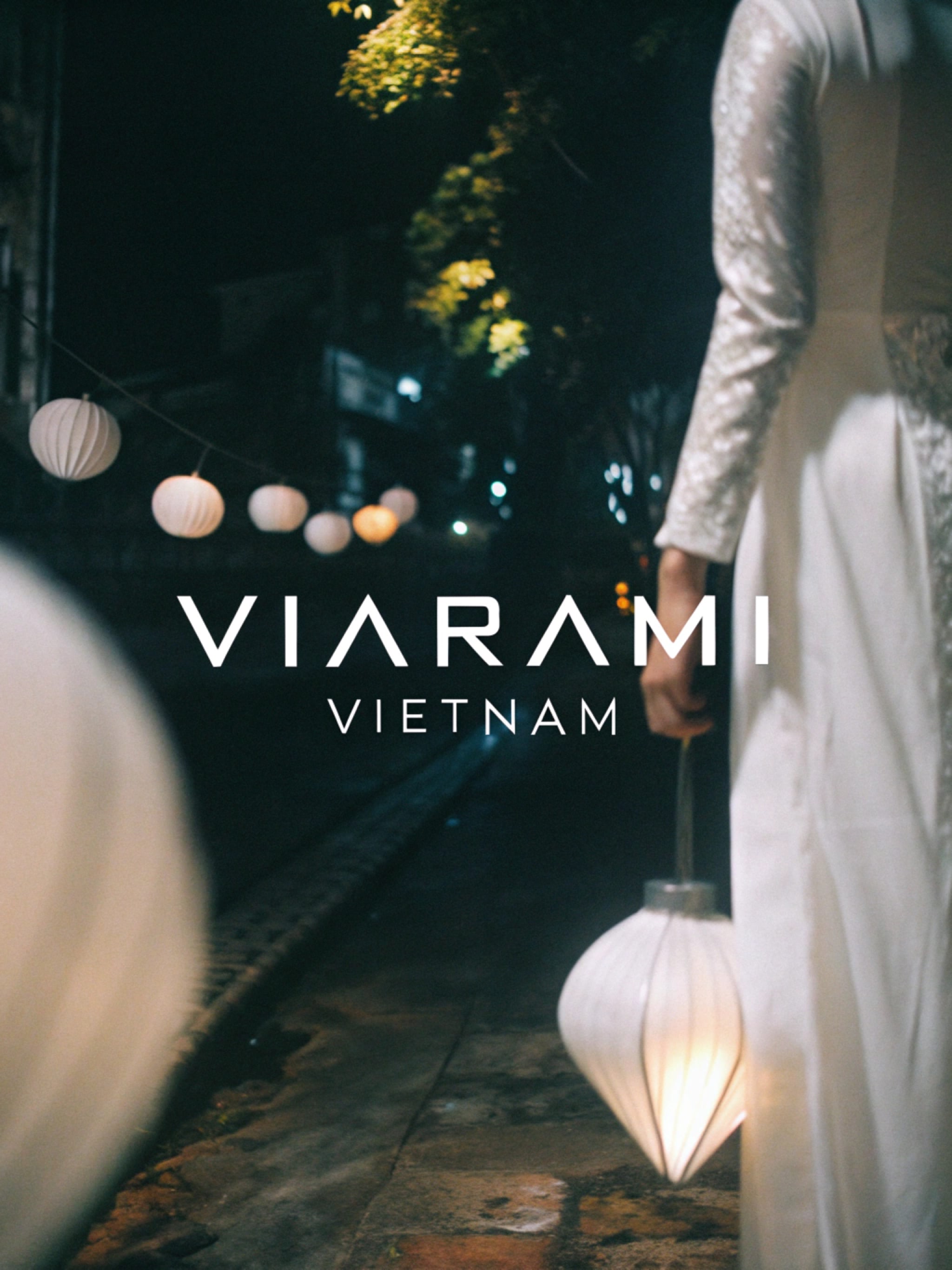 A woman in a white dress holds a lantern at night in Vietnam, with other lanterns in the background.