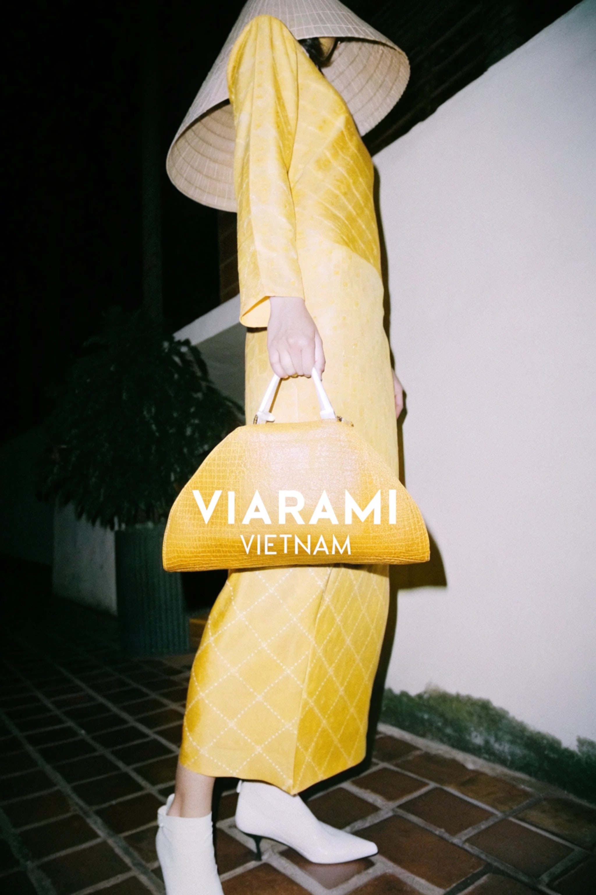 A person wearing a yellow dress and an Asian conical hat, holding a handbag.