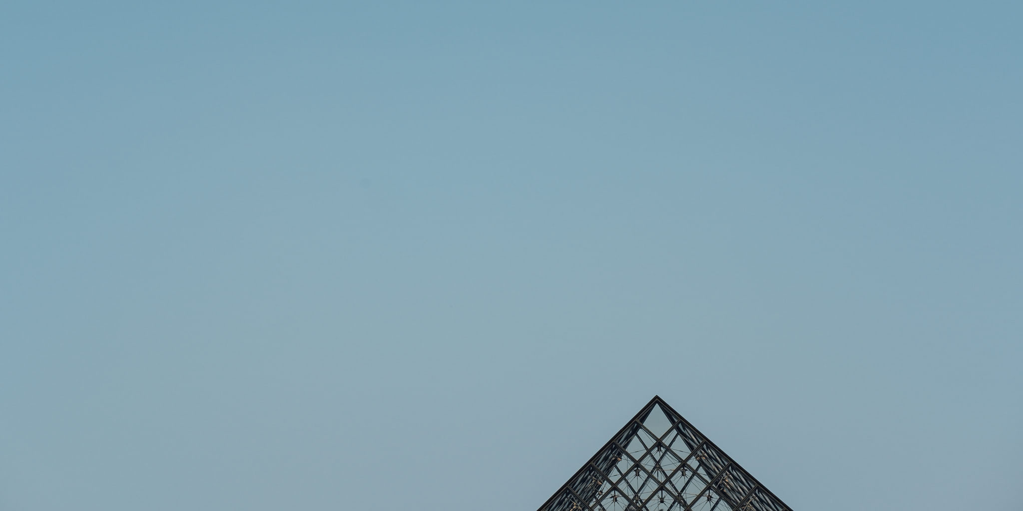 Glass pyramid against a blue sky. The pyramid is only partially visible at the bottom of the image.