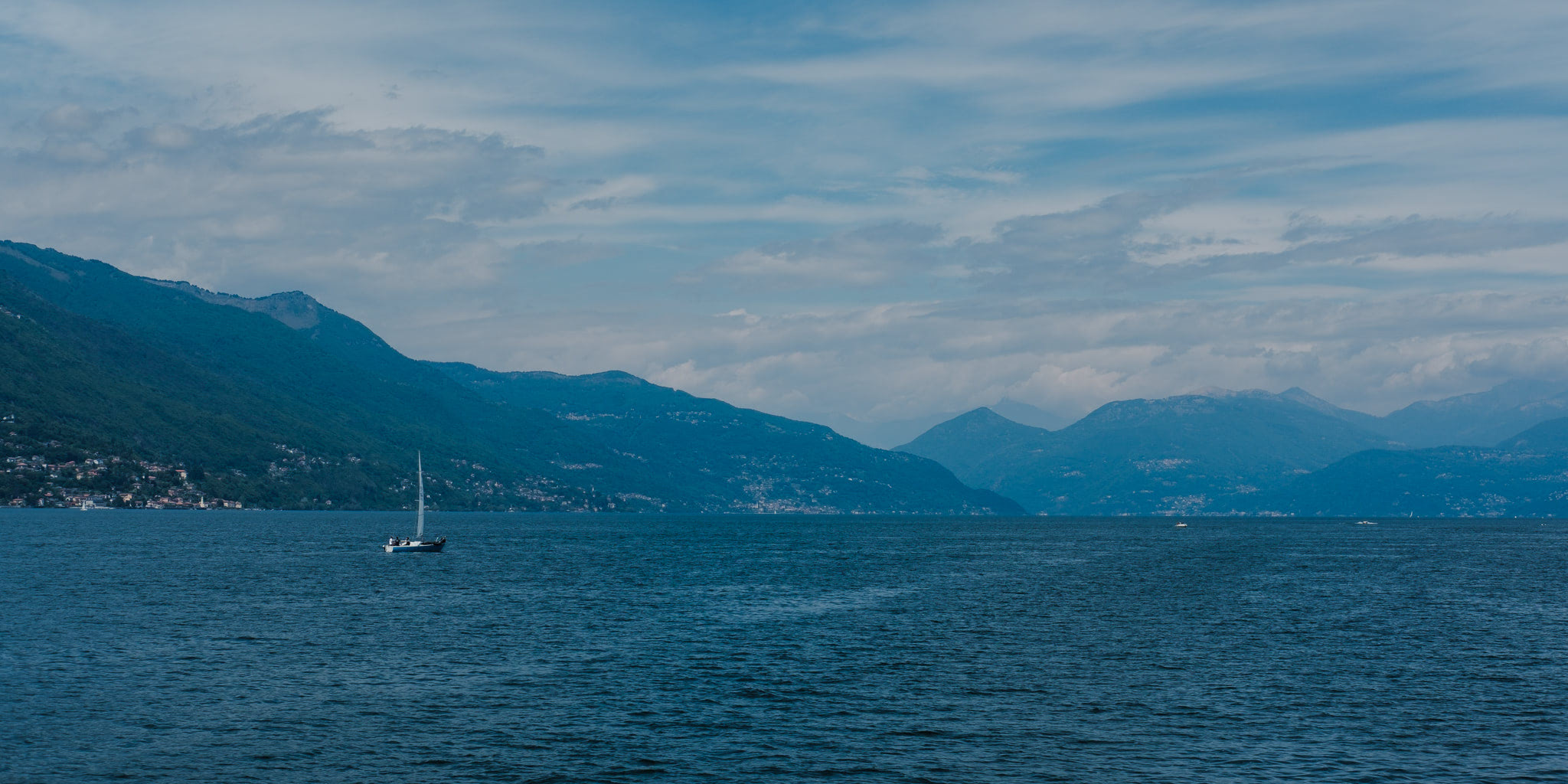 Sailboat on a lake with mountains in the background under a cloudy blue sky.