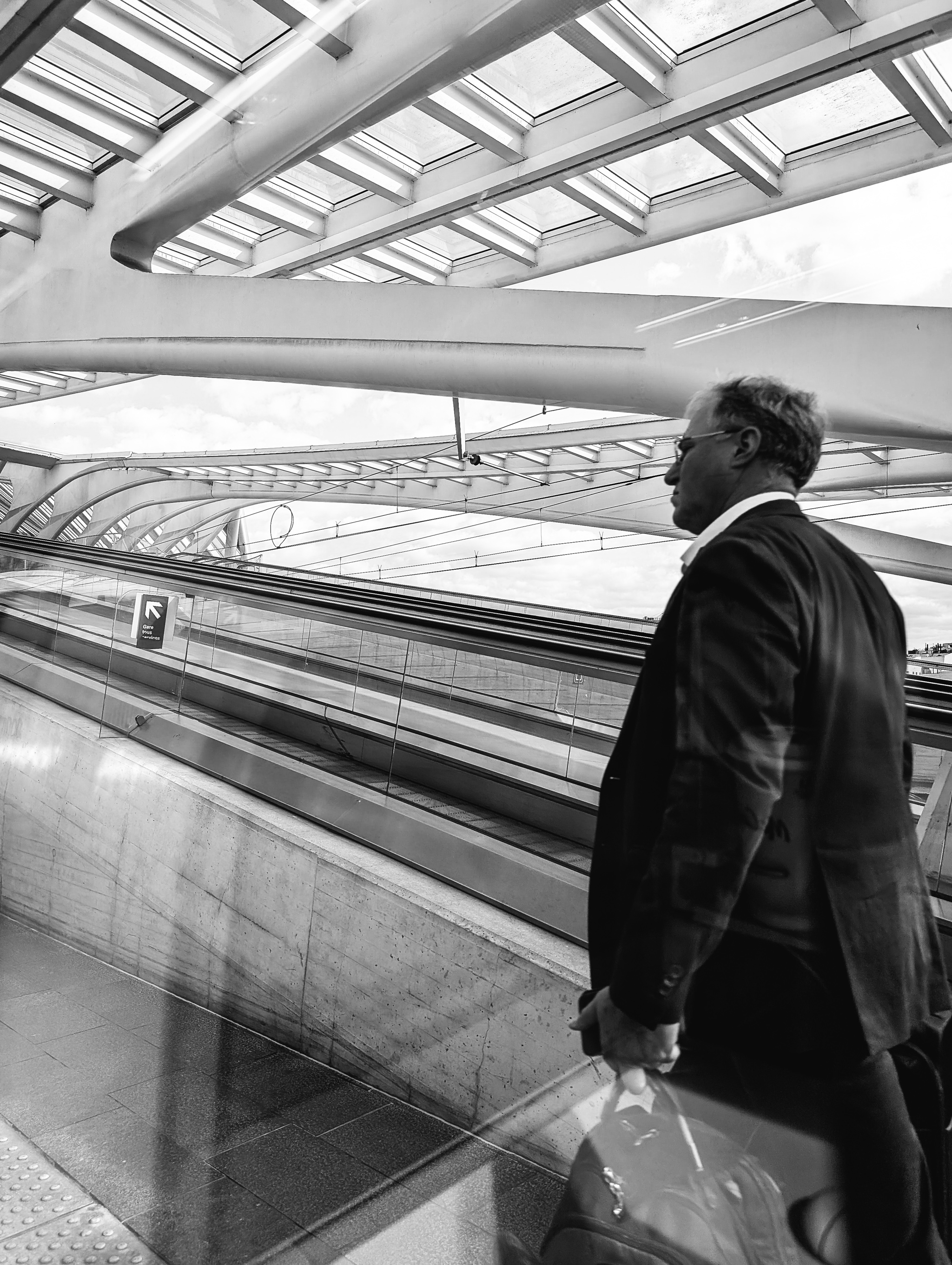 Black and white photo of a man in a suit walking down an escalator in a modern building.