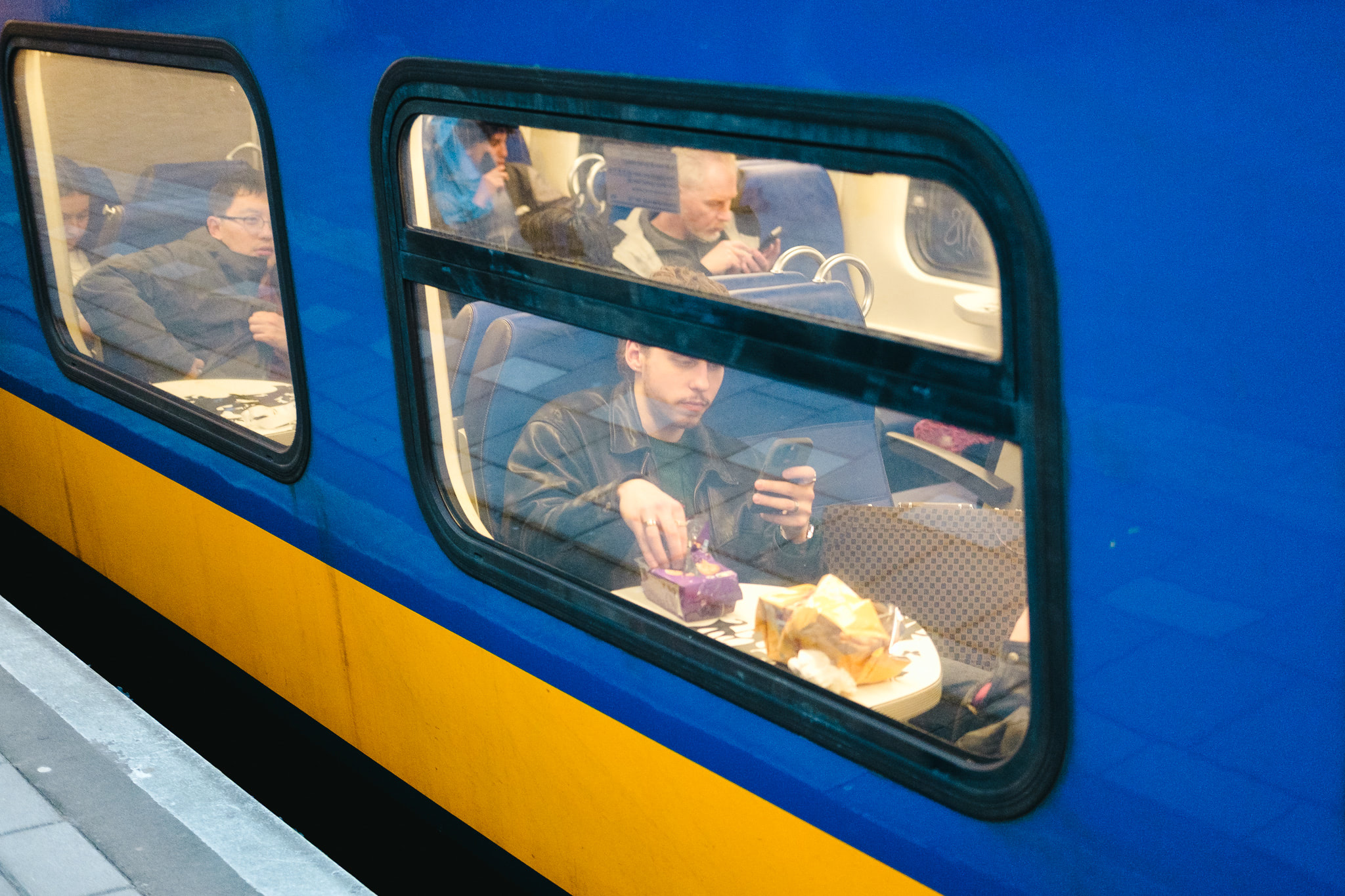 Man eating on train, using phone. Other passengers are visible.