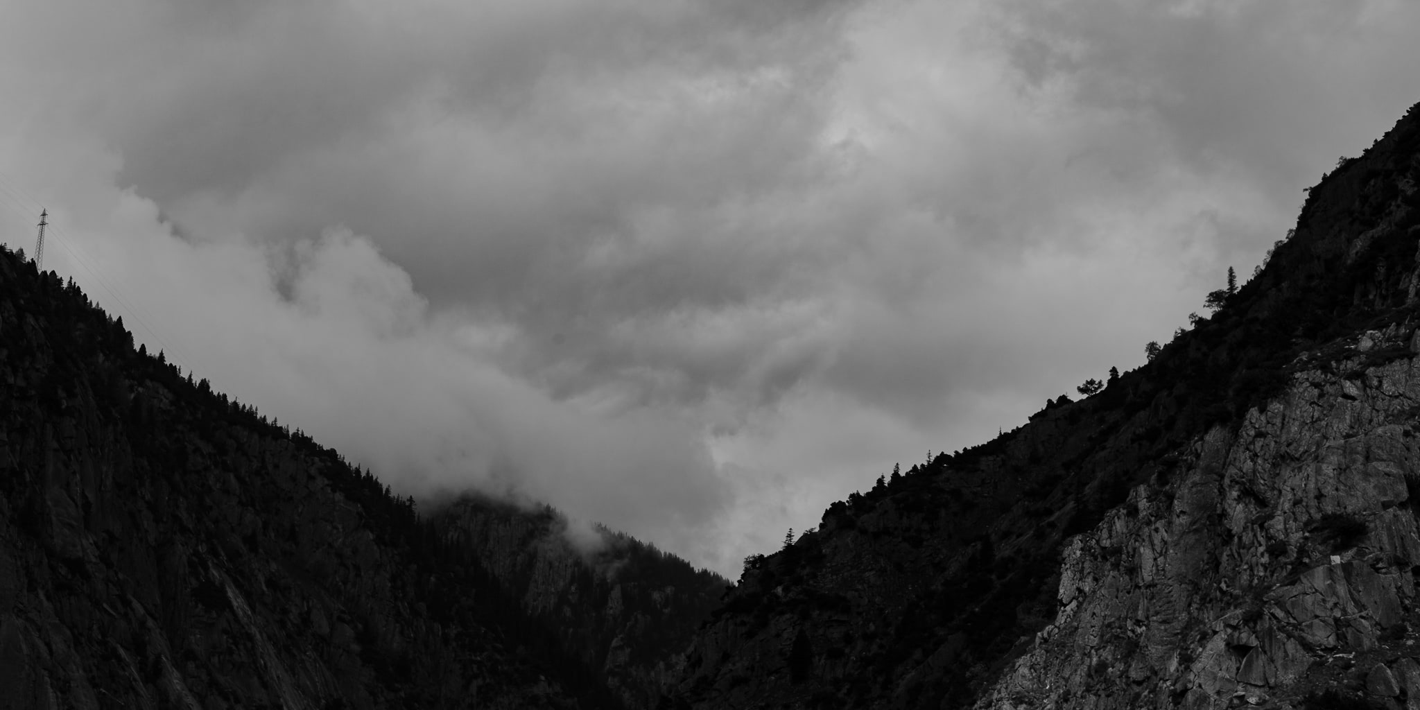 Black and white image of two mountain slopes converging, with clouds obscuring the peaks.