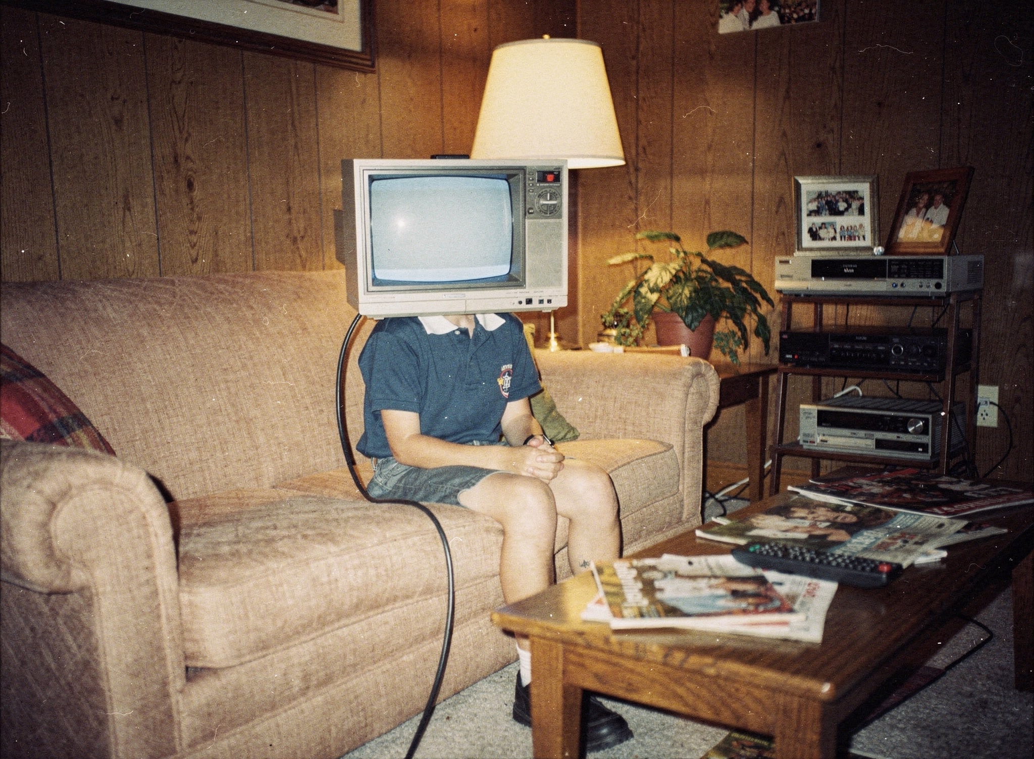 Person sitting on a sofa with a vintage television over their head in a wood-paneled living room.