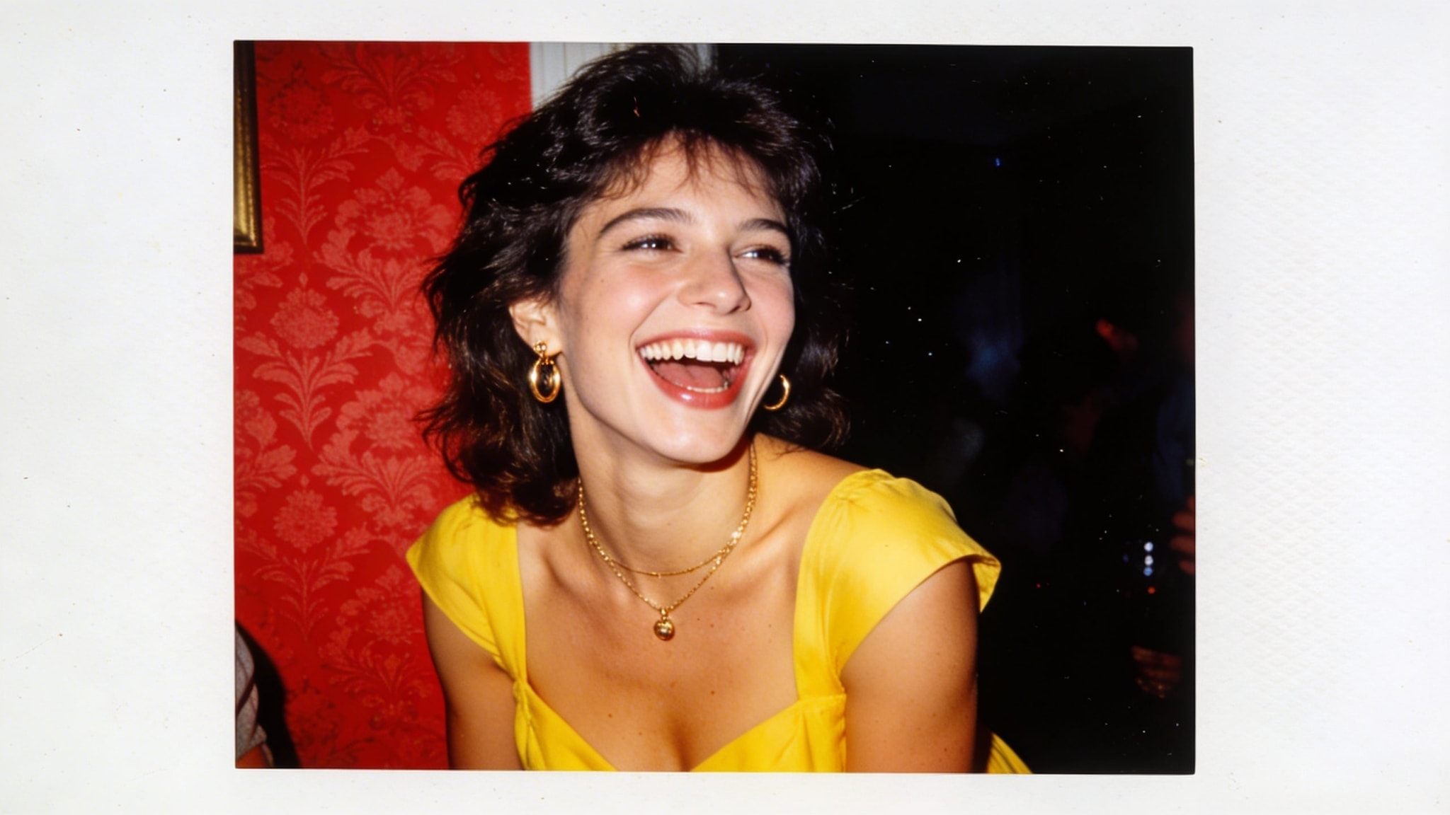 A woman in a bright yellow dress laughs at a 1970s house party, captured with a harsh on-camera flash against red wallpaper.