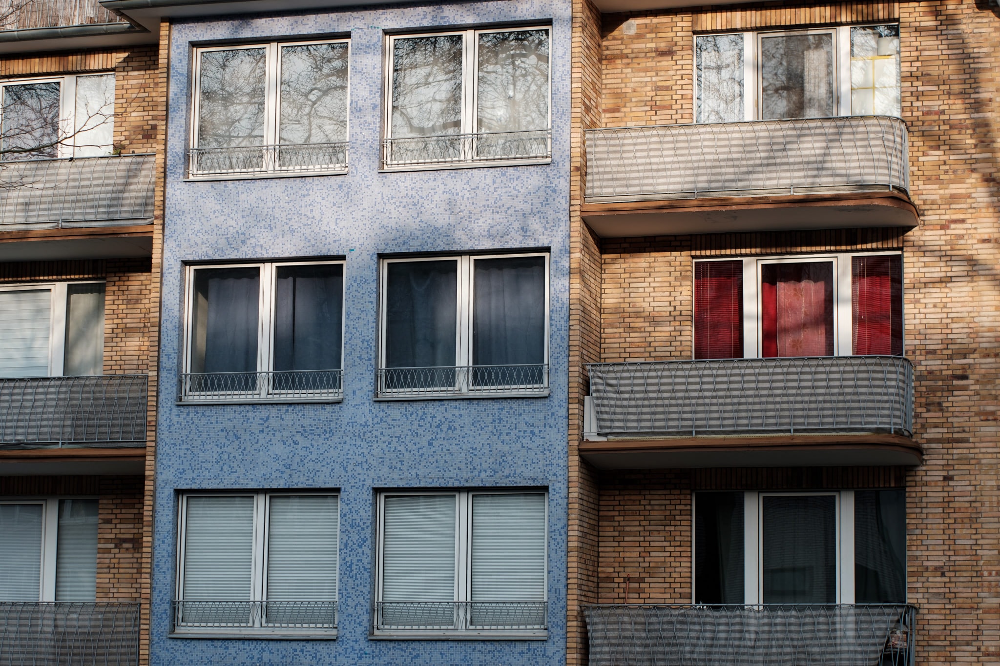 Exterior view of an apartment building facade featuring blue tiled accents, brown brickwork, and multiple balconies.