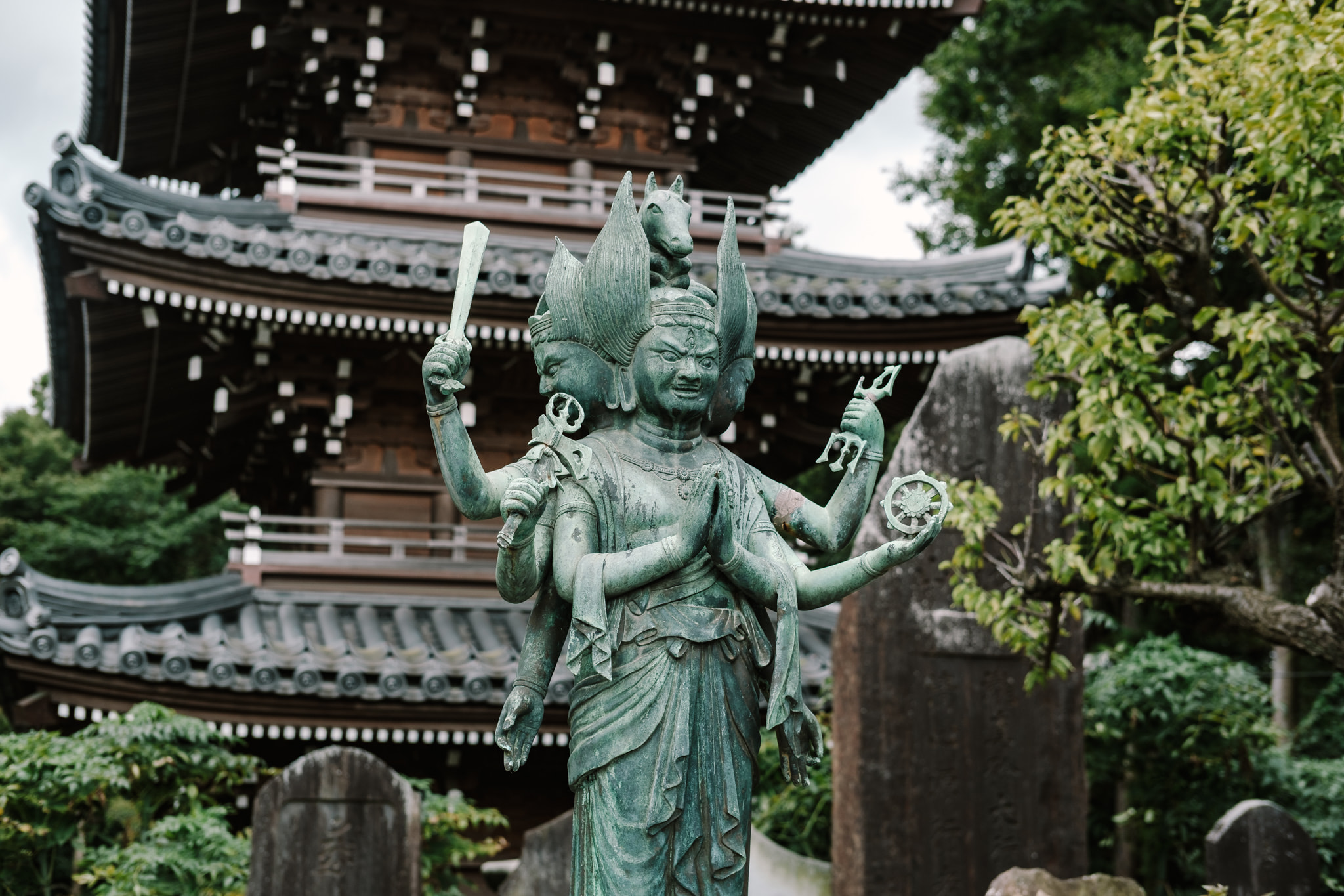 A bronze statue of Bato Kannon with multiple arms and heads in front of a Japanese pagoda.