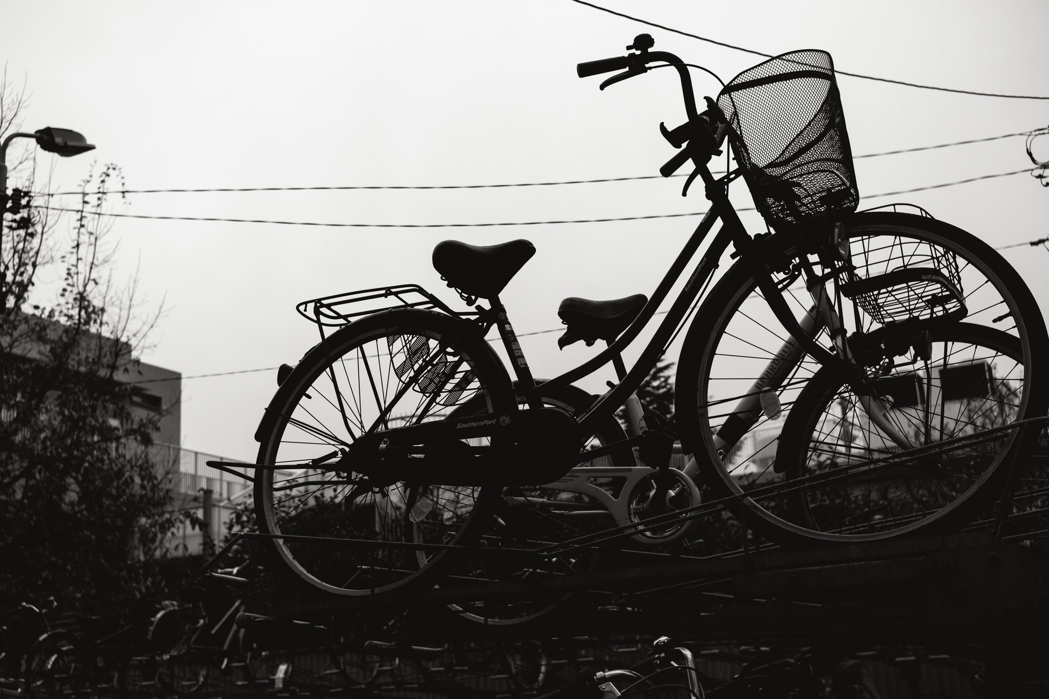 Silhouette of a parked bicycle with a basket against a grey sky.