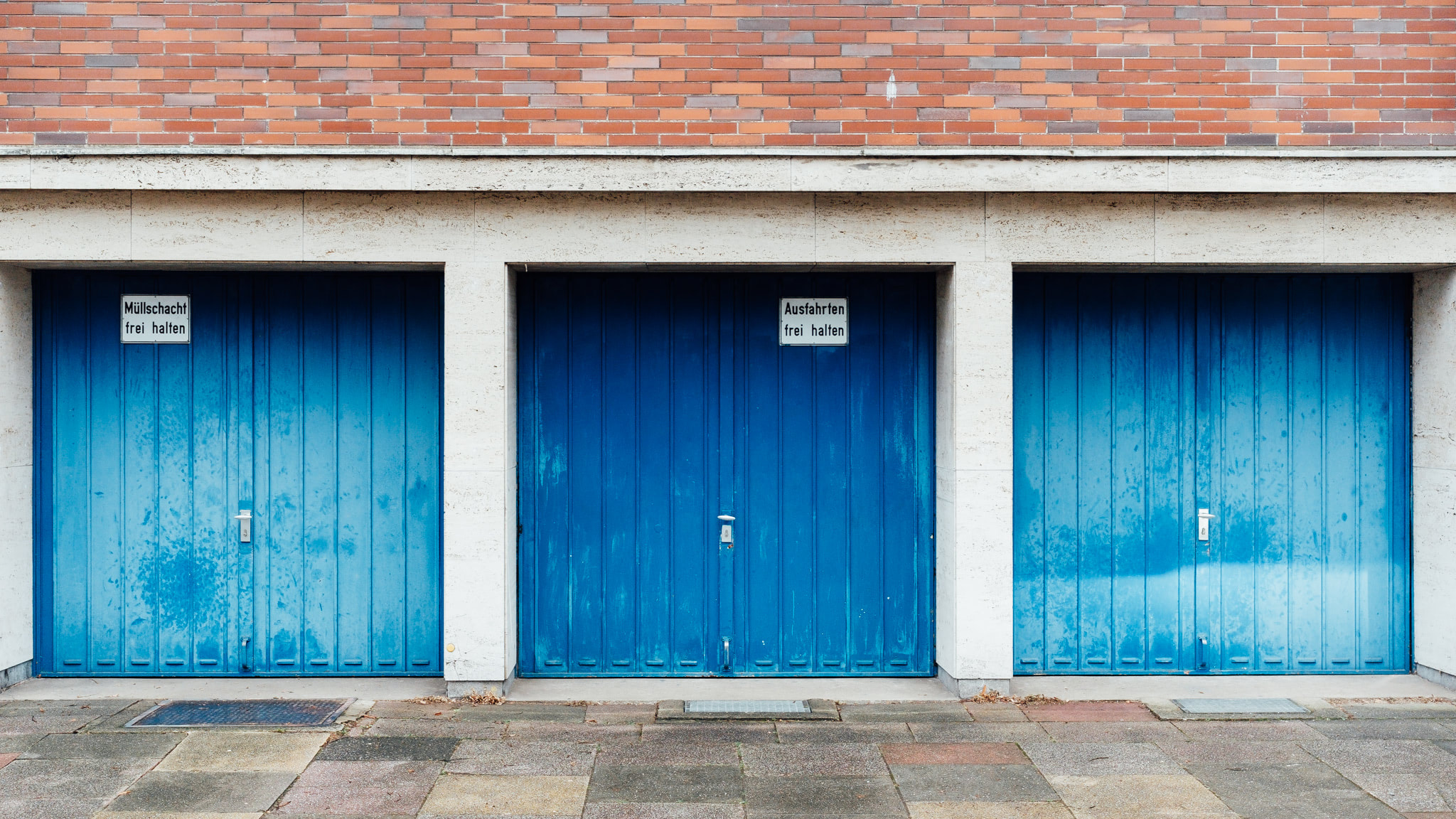 Three bright blue garage doors in a concrete and brick building.