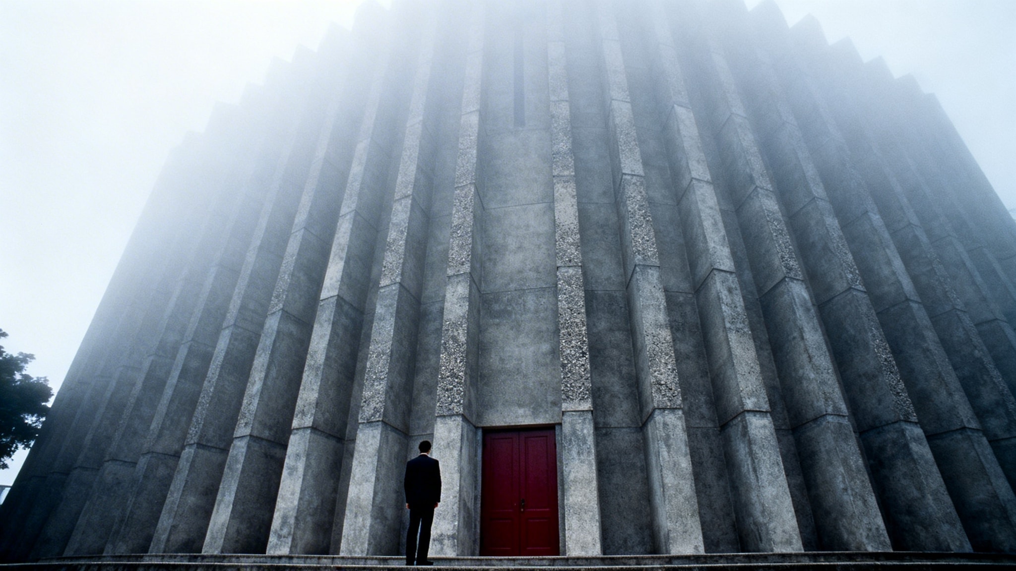 A 1965 Kodachrome photograph of the stark, geometric facade of the Chinese Methodist Church in North Point, featuring raw concrete columns and a red door in heavy fog.