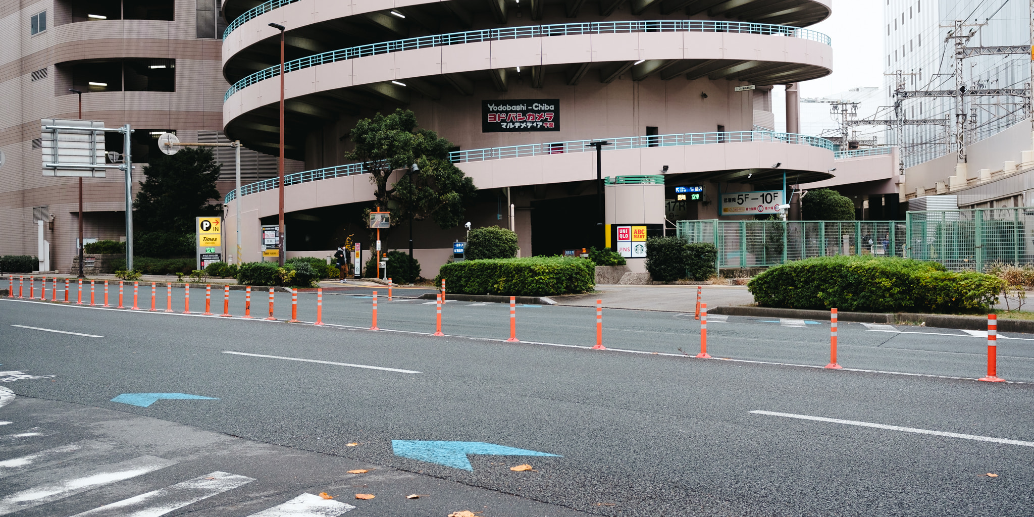 A multi-level cylindrical parking garage building situated near an asphalt road with orange traffic bollards in Chiba, Japan.