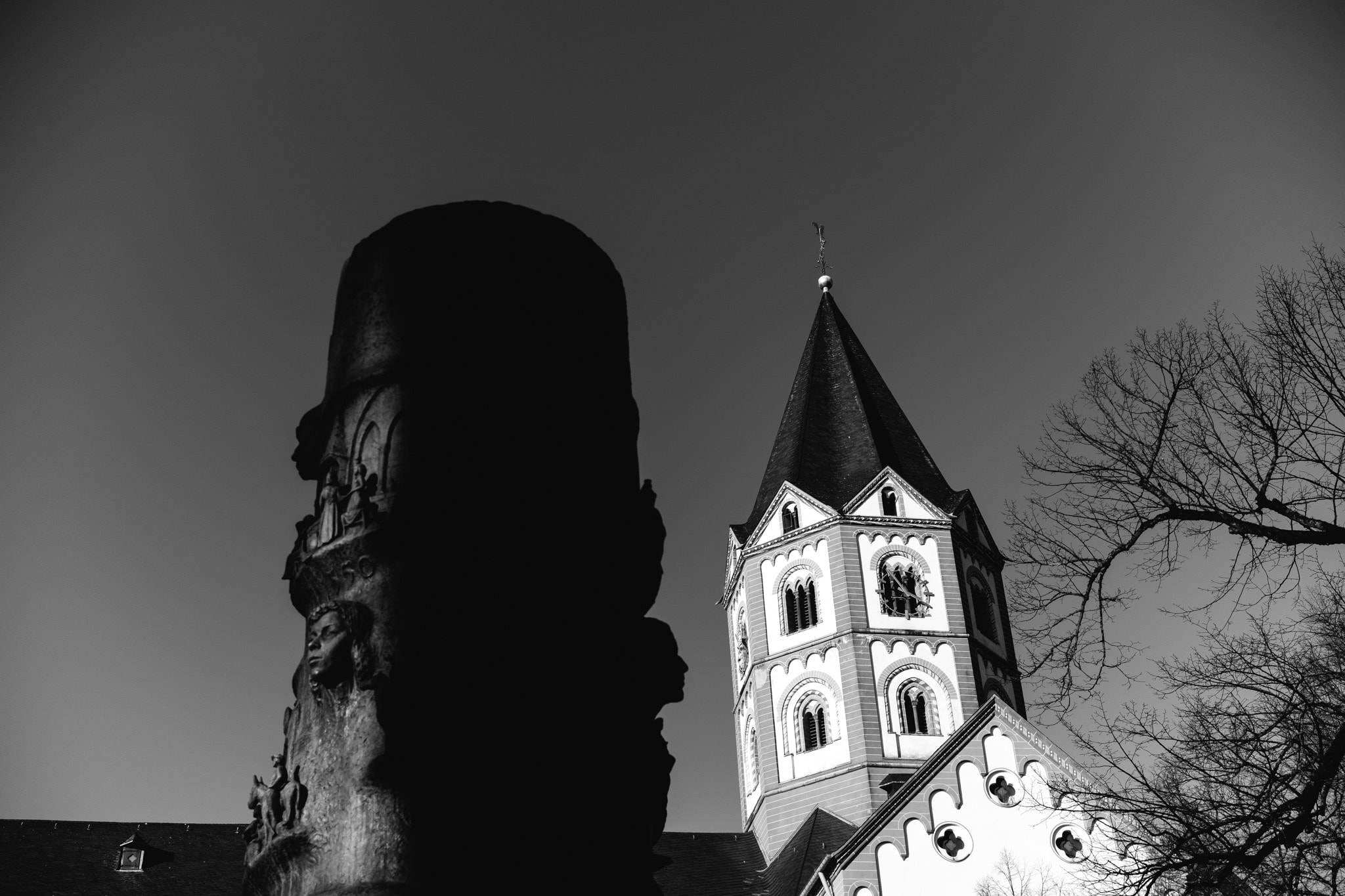 Black and white view of a church steeple and a carved stone monument pillar.