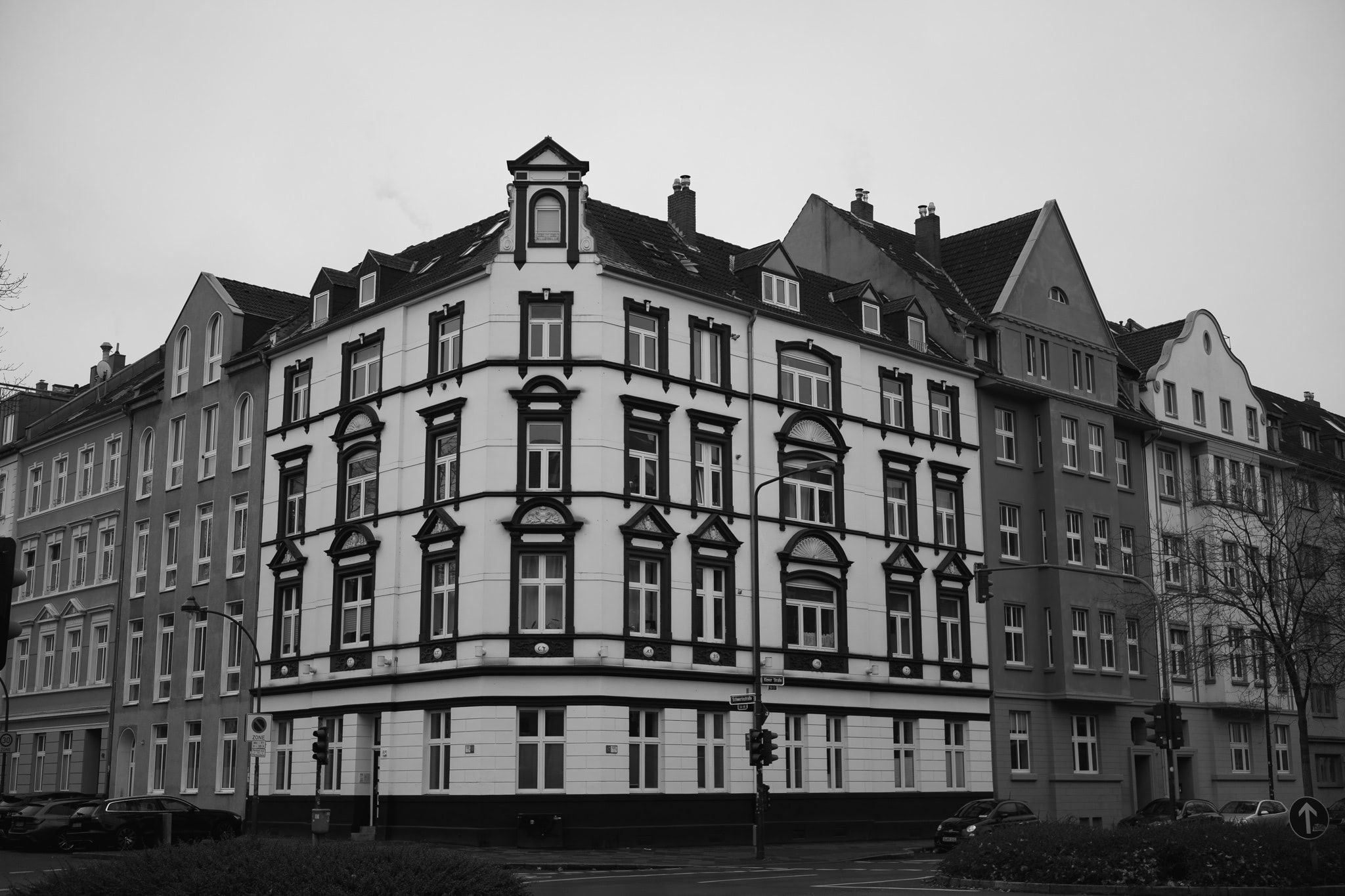 A black and white street view of a corner apartment building with ornate facades and classical architecture in an urban setting.