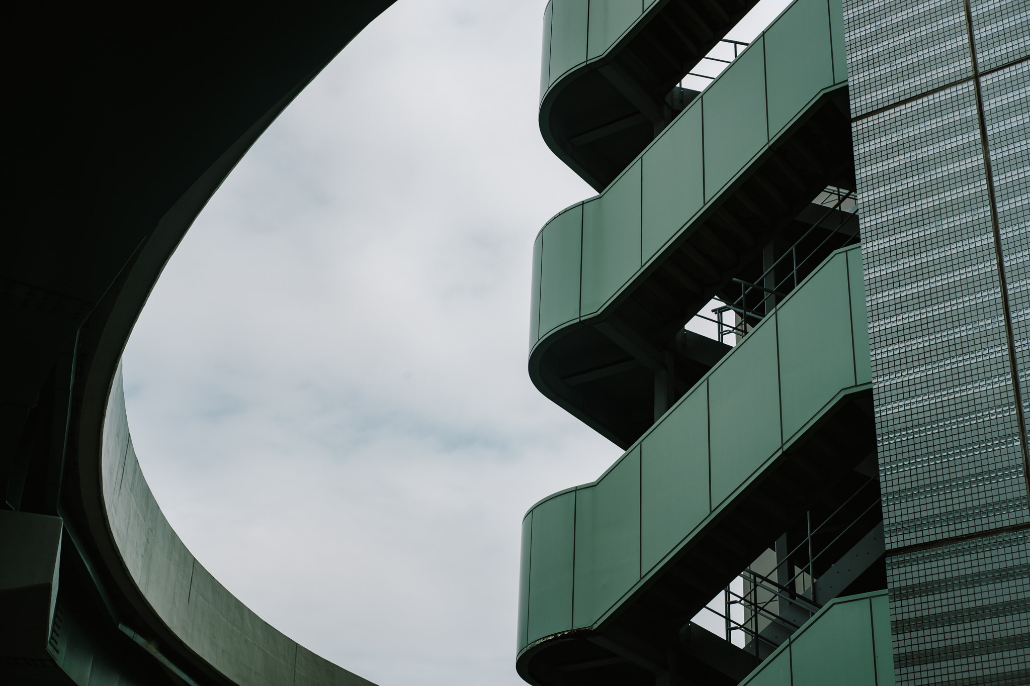 Architectural details of a curved green building structure against a cloudy sky.