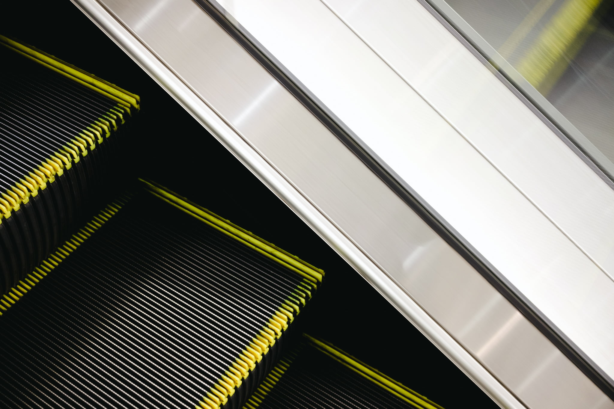 Close-up view of a metal escalator step with yellow safety trim and brushed steel railing.