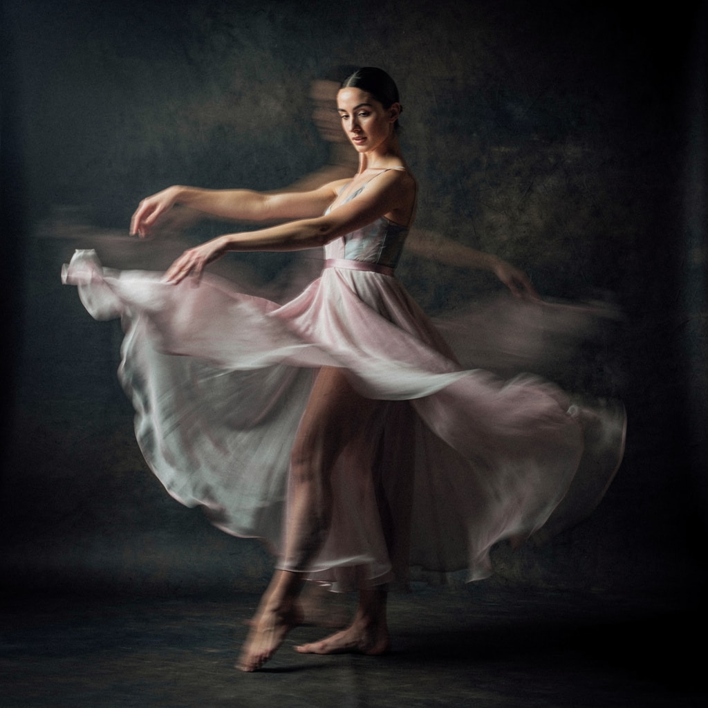 Fine art portrait of a contemporary dancer in a translucent silk dress with motion blur against a dark backdrop