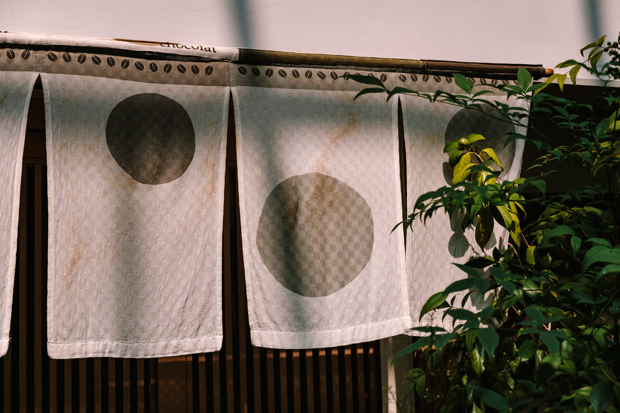 A Japanese noren curtain featuring minimalist circular patterns hanging over a wooden storefront entrance.