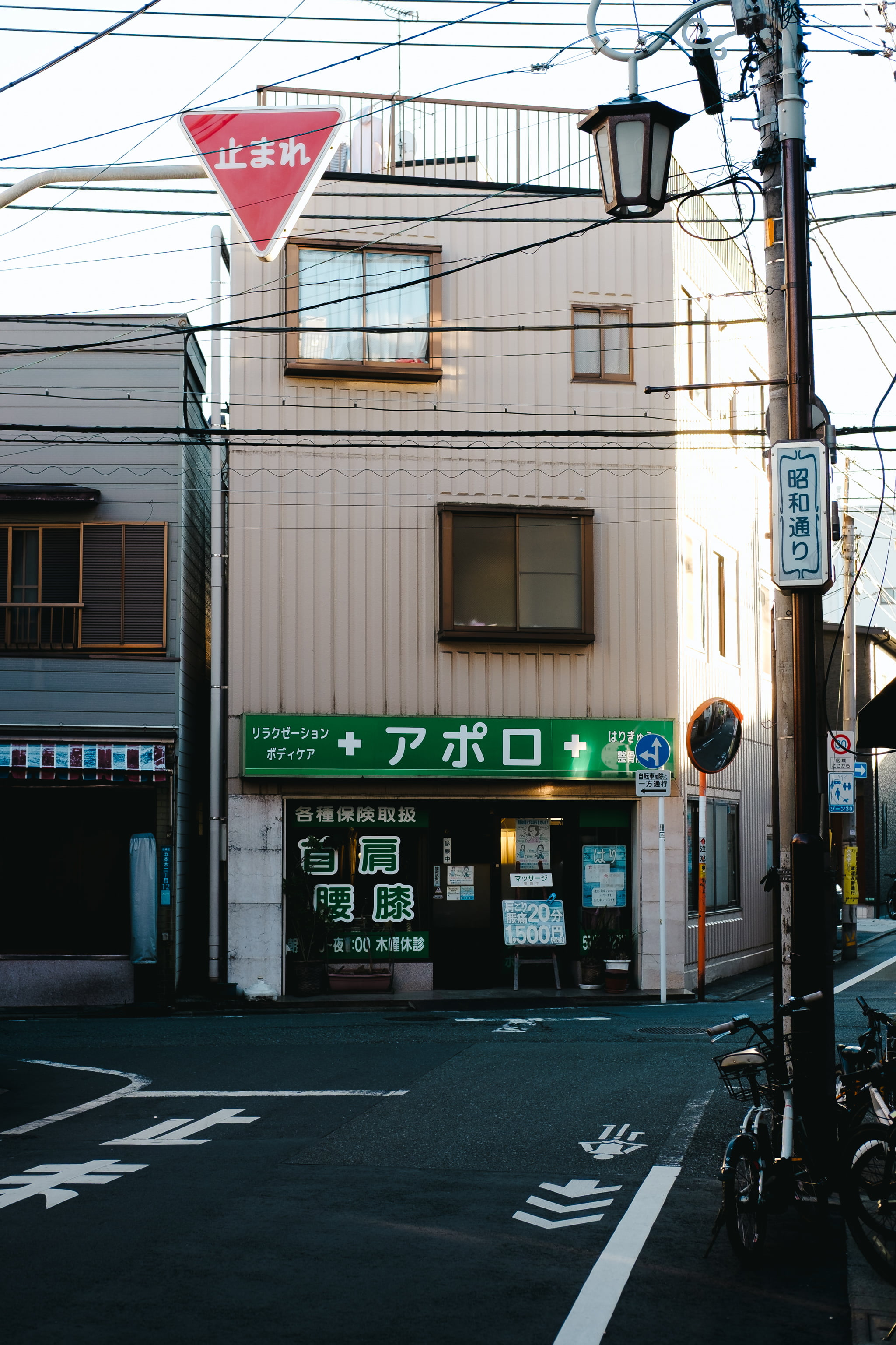 A quiet Japanese street corner featuring a massage clinic building with signage and overhead utility lines.