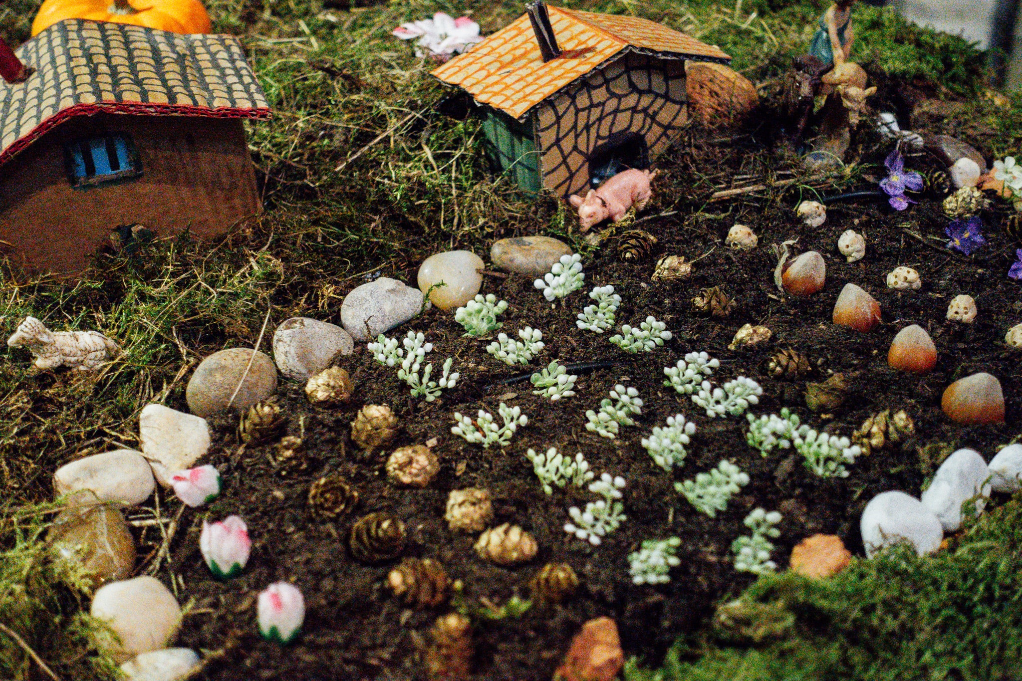 A miniature garden scene with cardboard houses and tiny animal figurines in a mossy landscape.