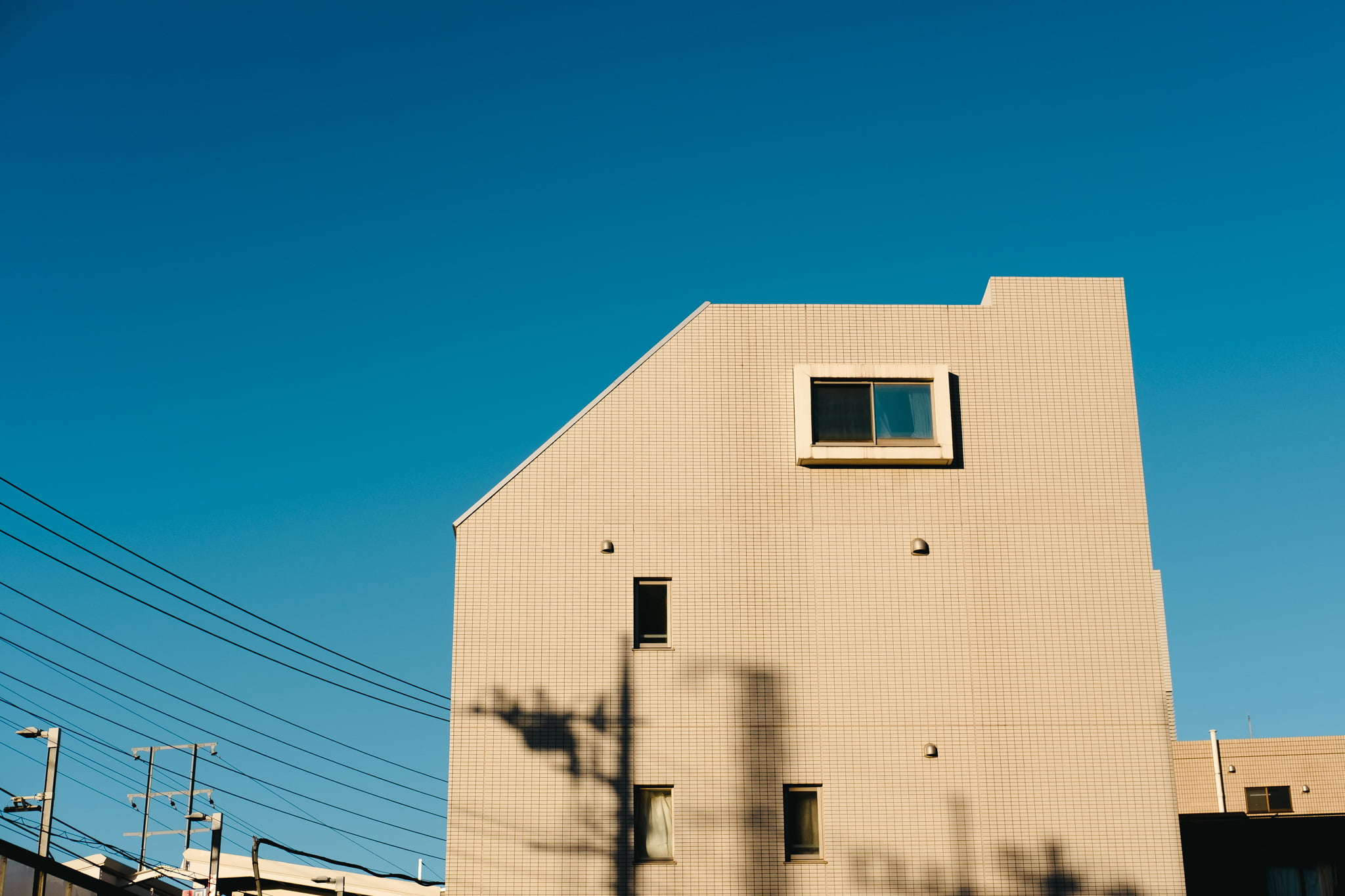 Modern tan tiled building exterior with geometric roofline against a clear blue sky