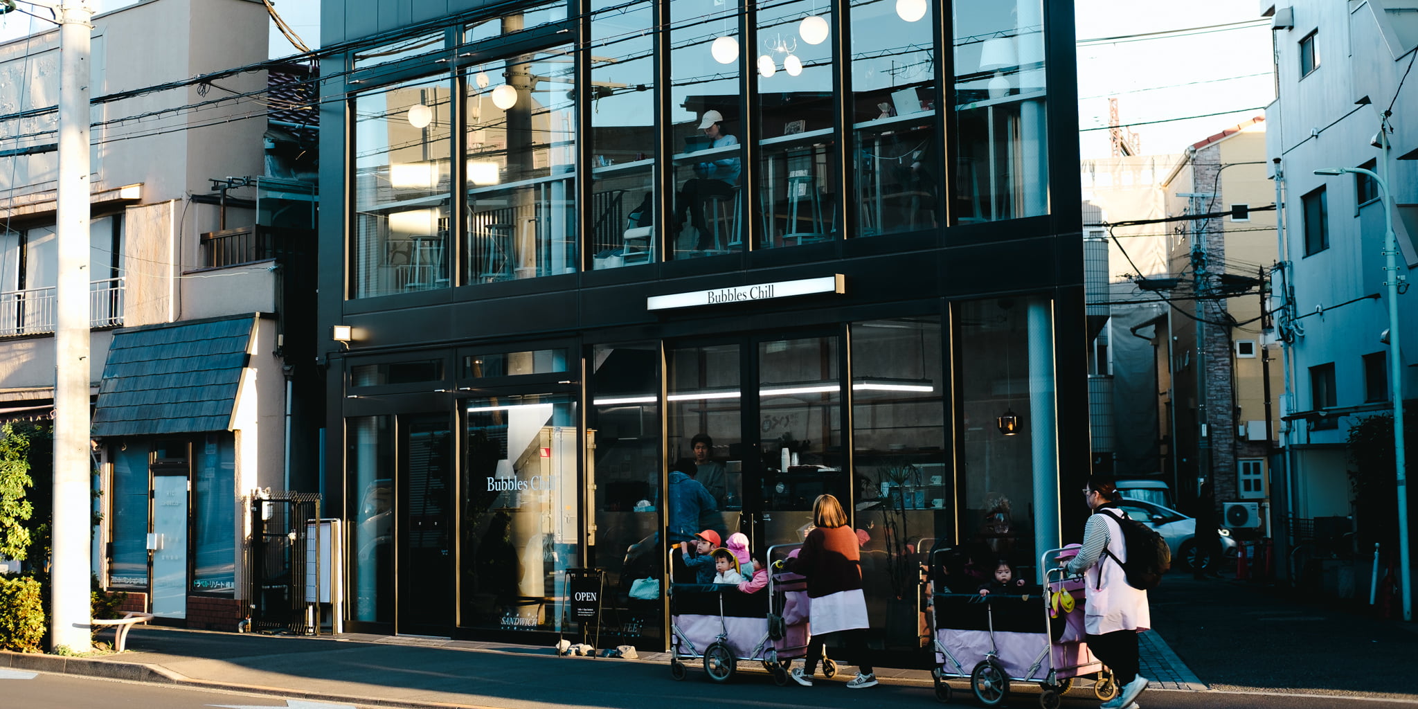 Modern glass building café in a Japanese town with people pushing strollers on the sidewalk.