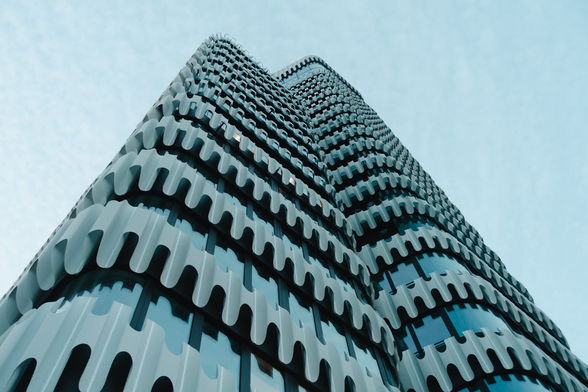 Low-angle view of a modern skyscraper with a white wave-like facade against a blue sky.