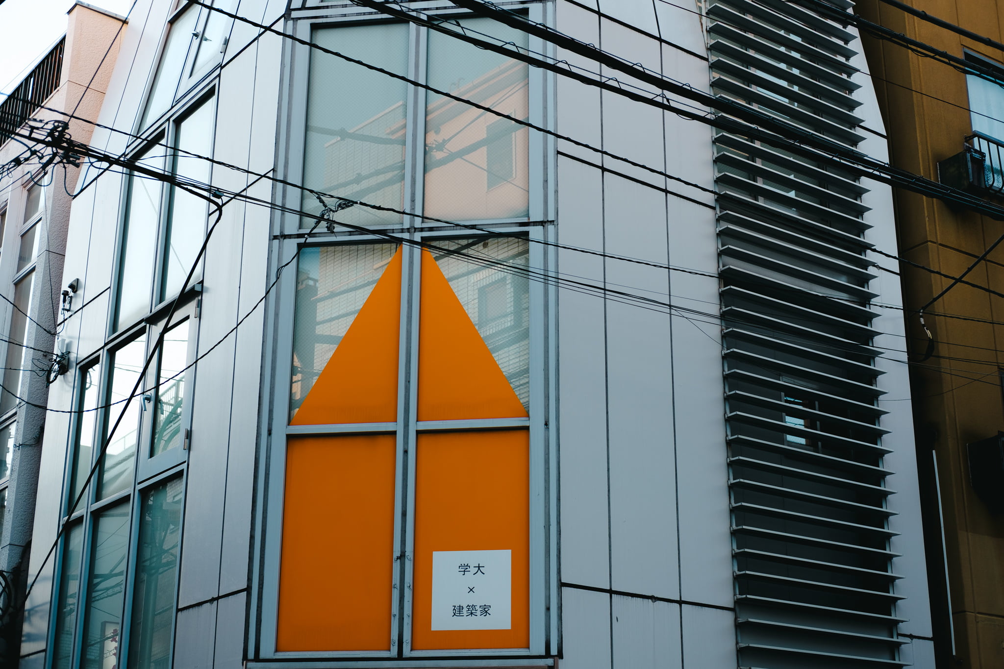Modern building facade with bright orange triangular signage and architectural detailing in an urban setting.