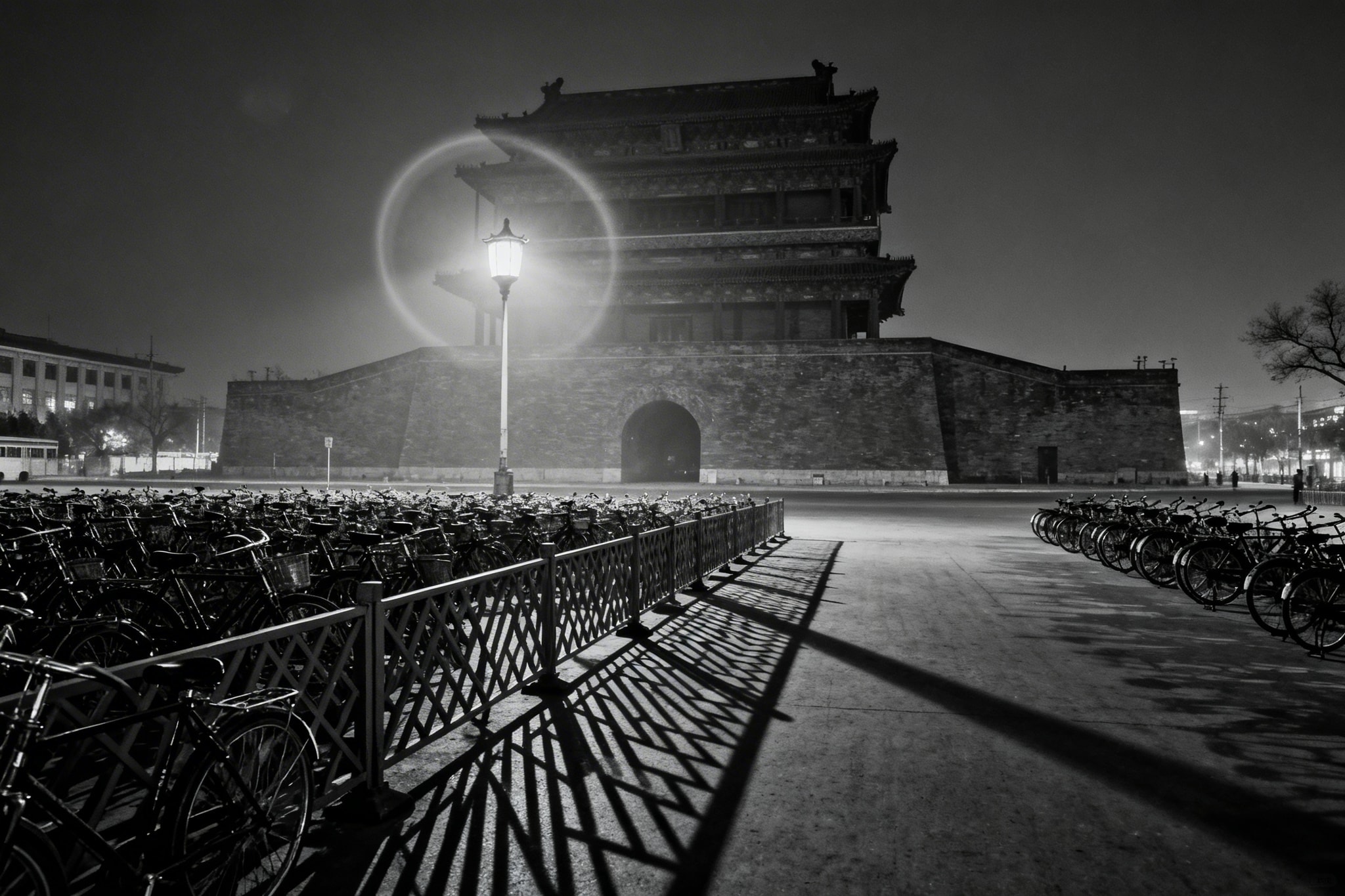 Black and white night photograph of Qianmen Gate in 1960s Beijing, lit by a single streetlamp with parked bicycles in foreground