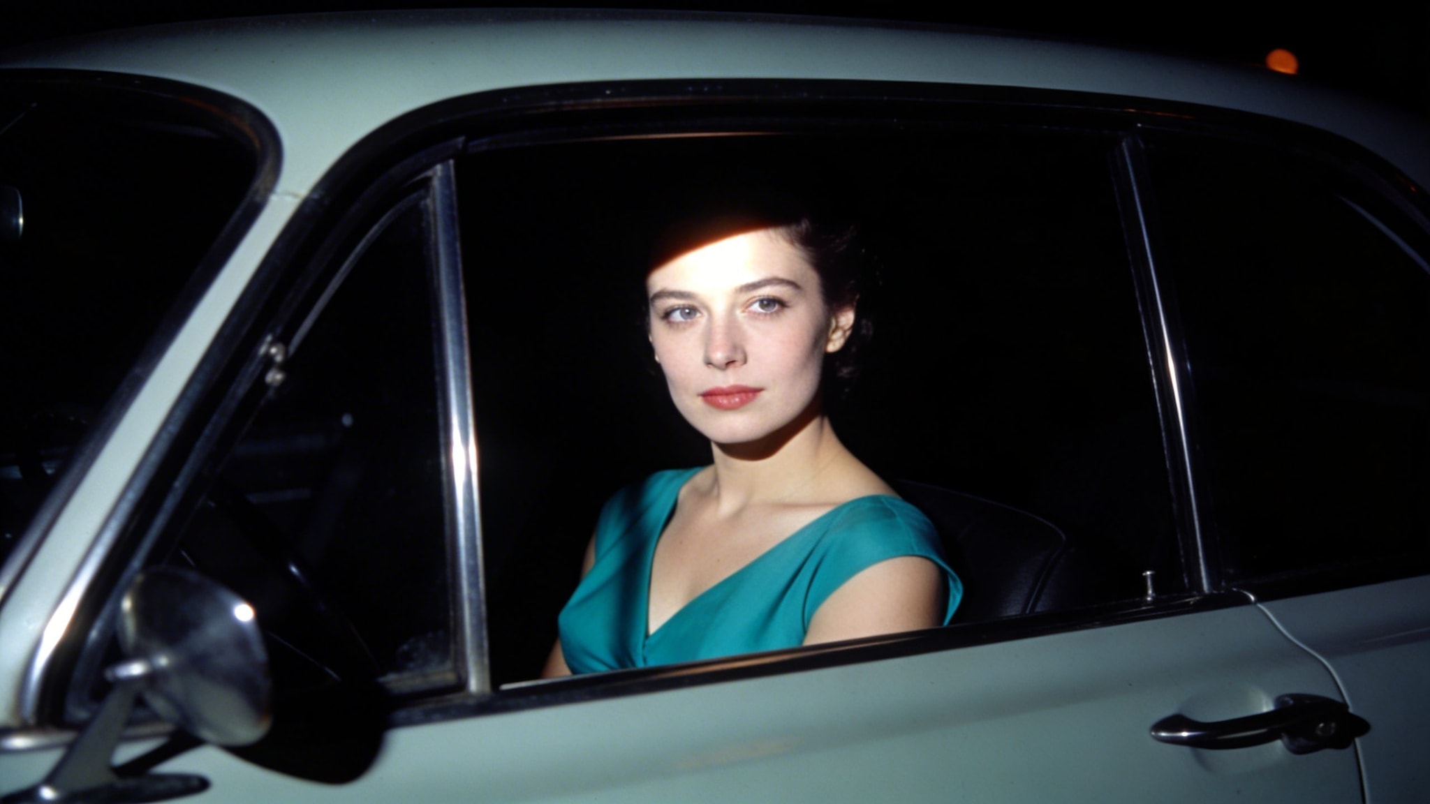 1950s woman in teal dress illuminated by flash in dark car interior