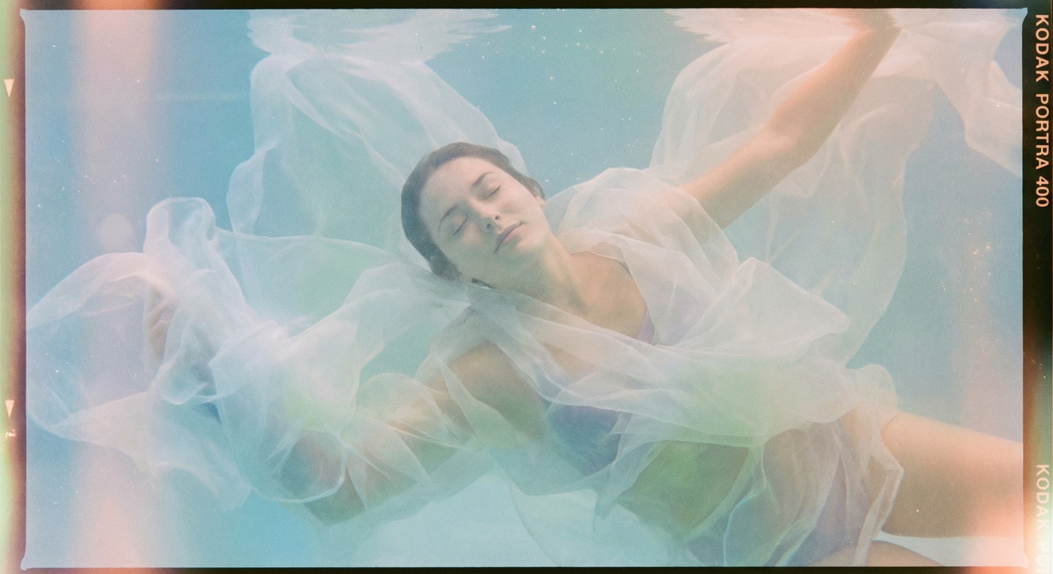 Serene person floating underwater in weightless white fabric, shot on film with soft pastel colors.