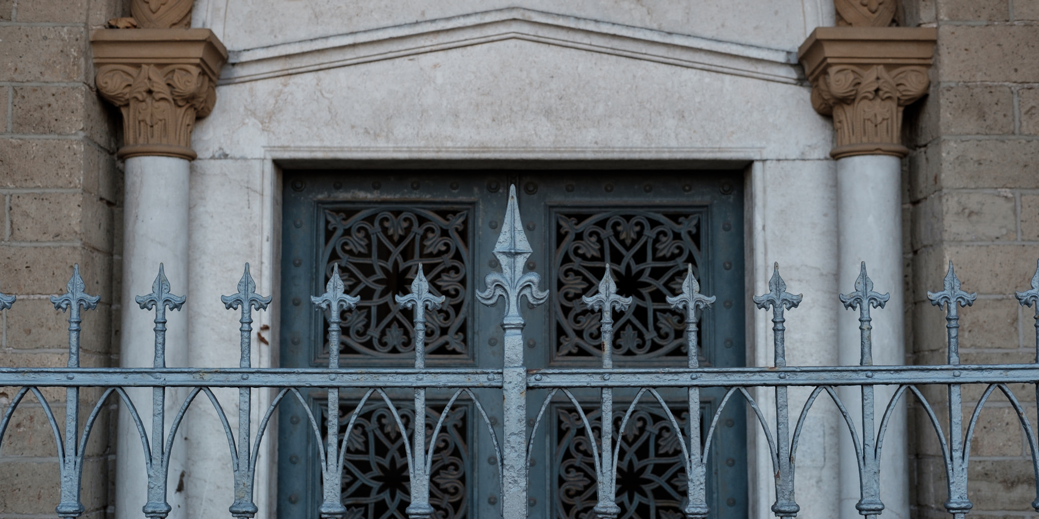 A close-up view of an ornate metal gate protecting a decorative stone door frame with classical columns.