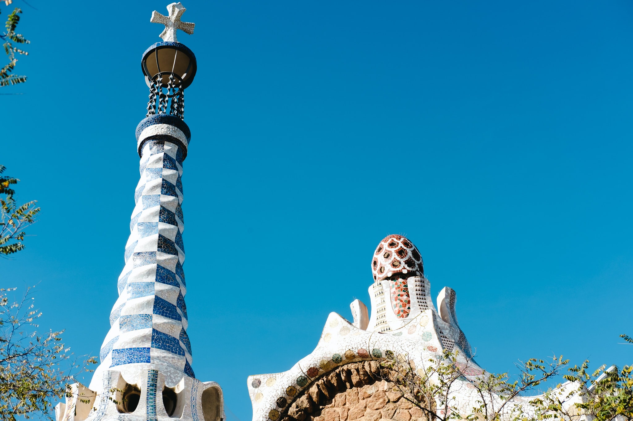 Architectural detail of Park Guell towers with blue mosaic tiles against a clear blue sky