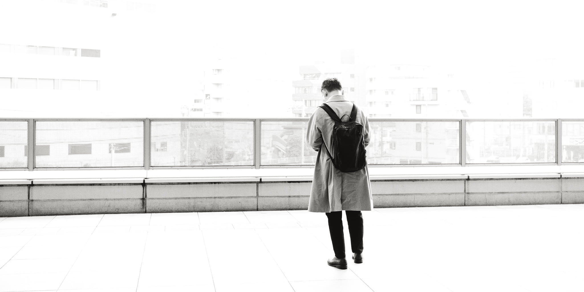 A person standing alone on a high-key, brightly lit balcony overlooking a cityscape.
