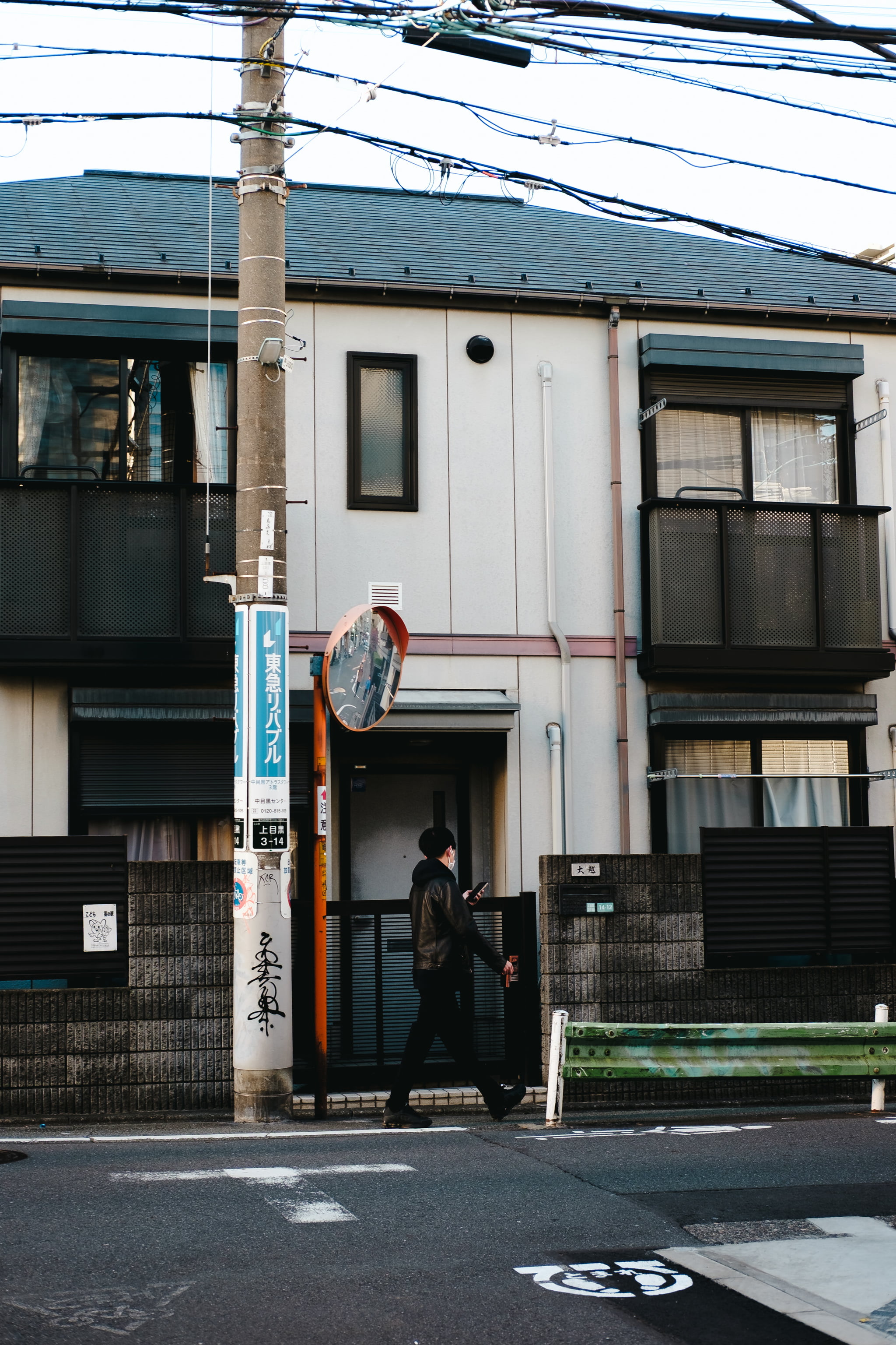 A person walking past a suburban Japanese house with a utility pole in the foreground.