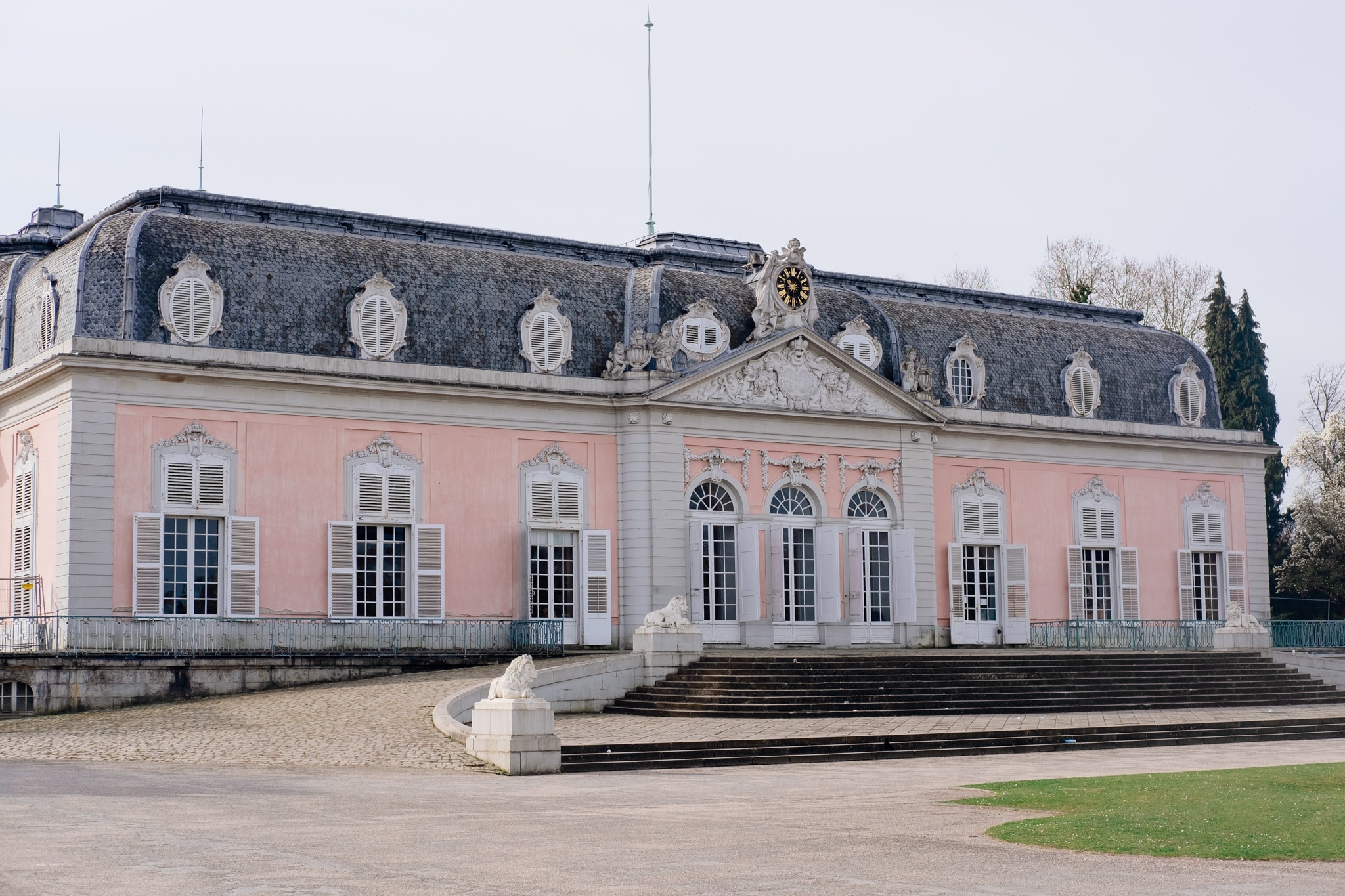 Exterior of a pink rococo palace with white shutters and a grey mansard roof.