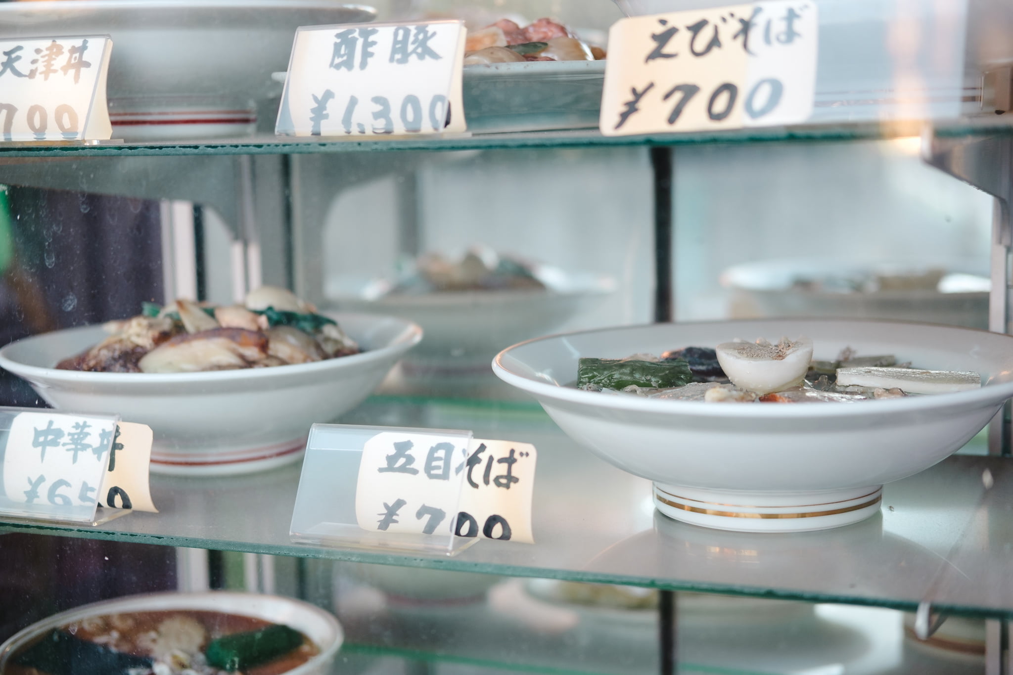 Plastic food models on display in a restaurant window with Japanese price tags.