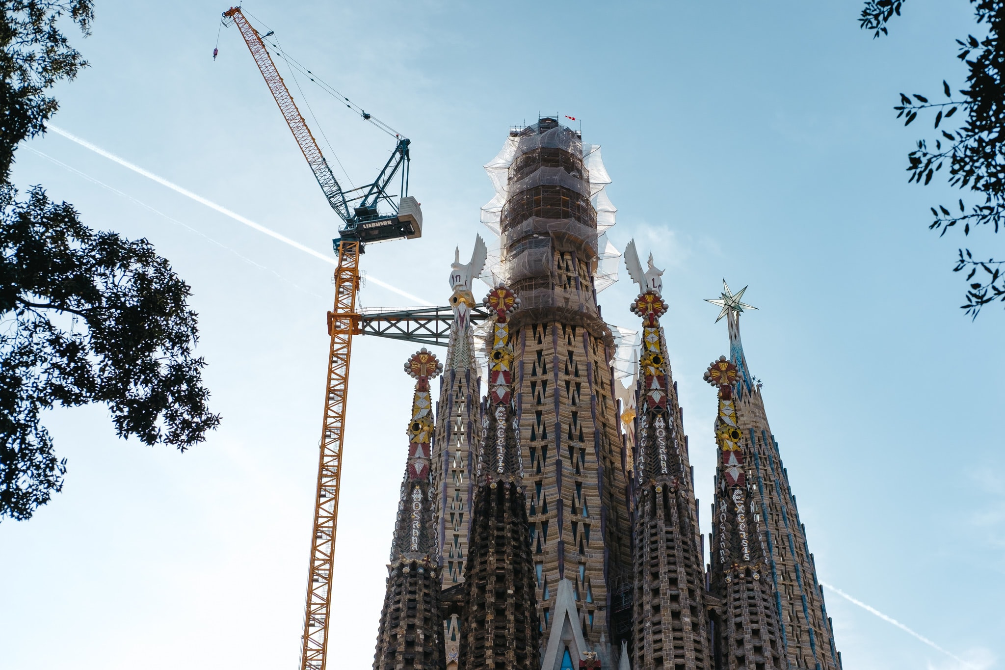 A low-angle view of the Sagrada Familia basilica under construction with a large yellow tower crane.