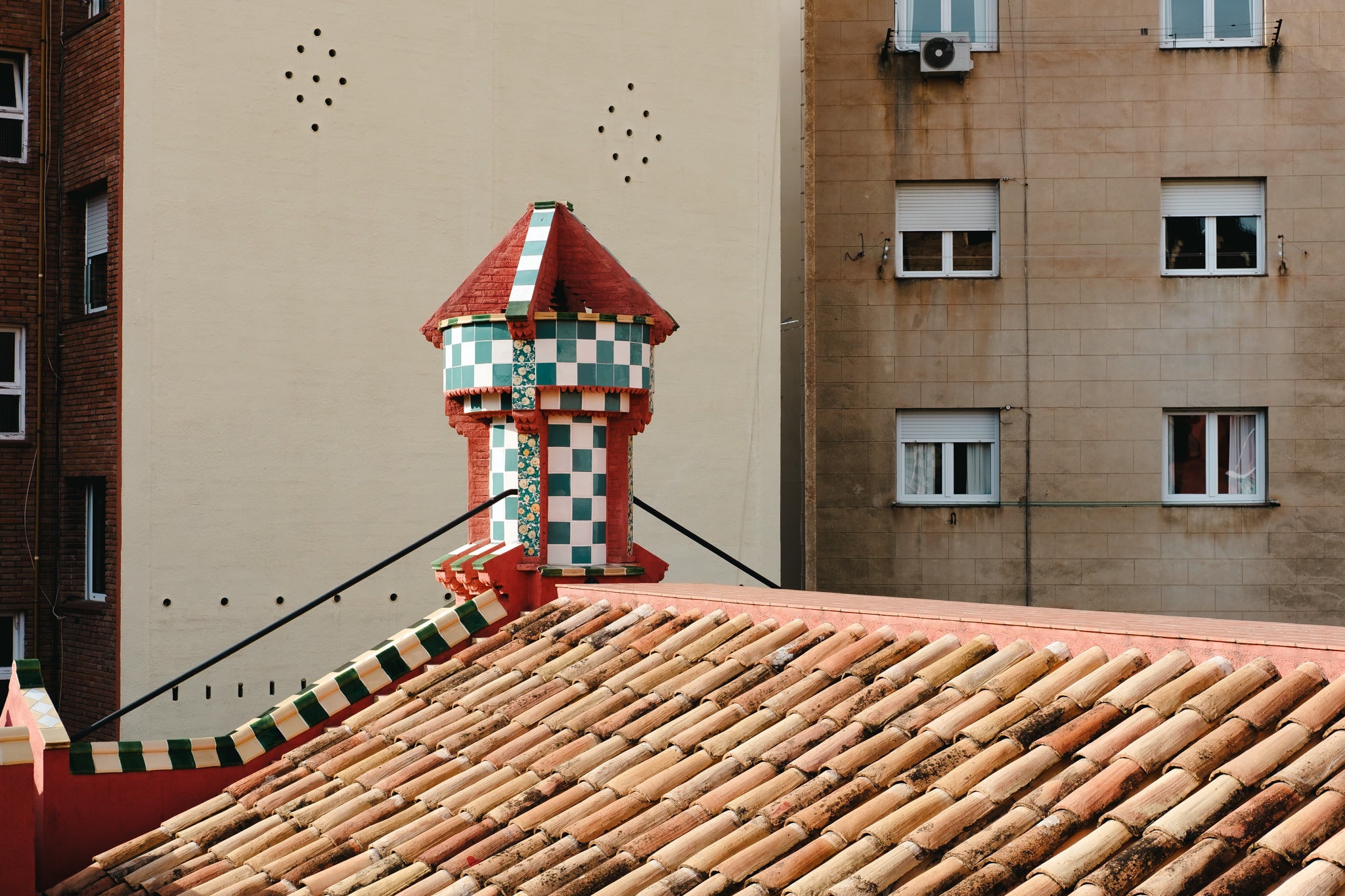 A decorative tiled chimney structure on a terracotta roof against urban apartment buildings.