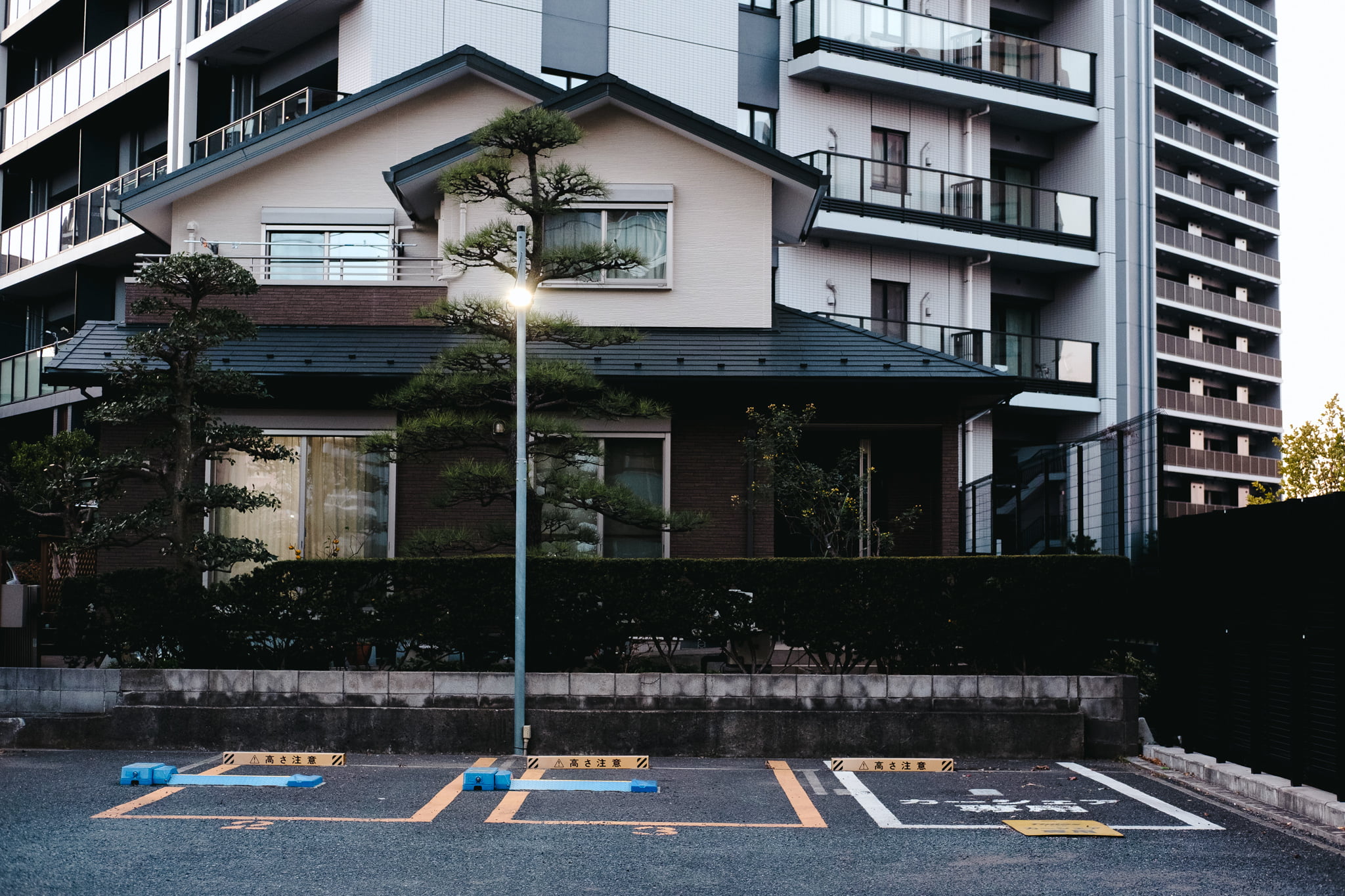 A small traditional Japanese house contrasted against a modern high-rise apartment building at dusk.