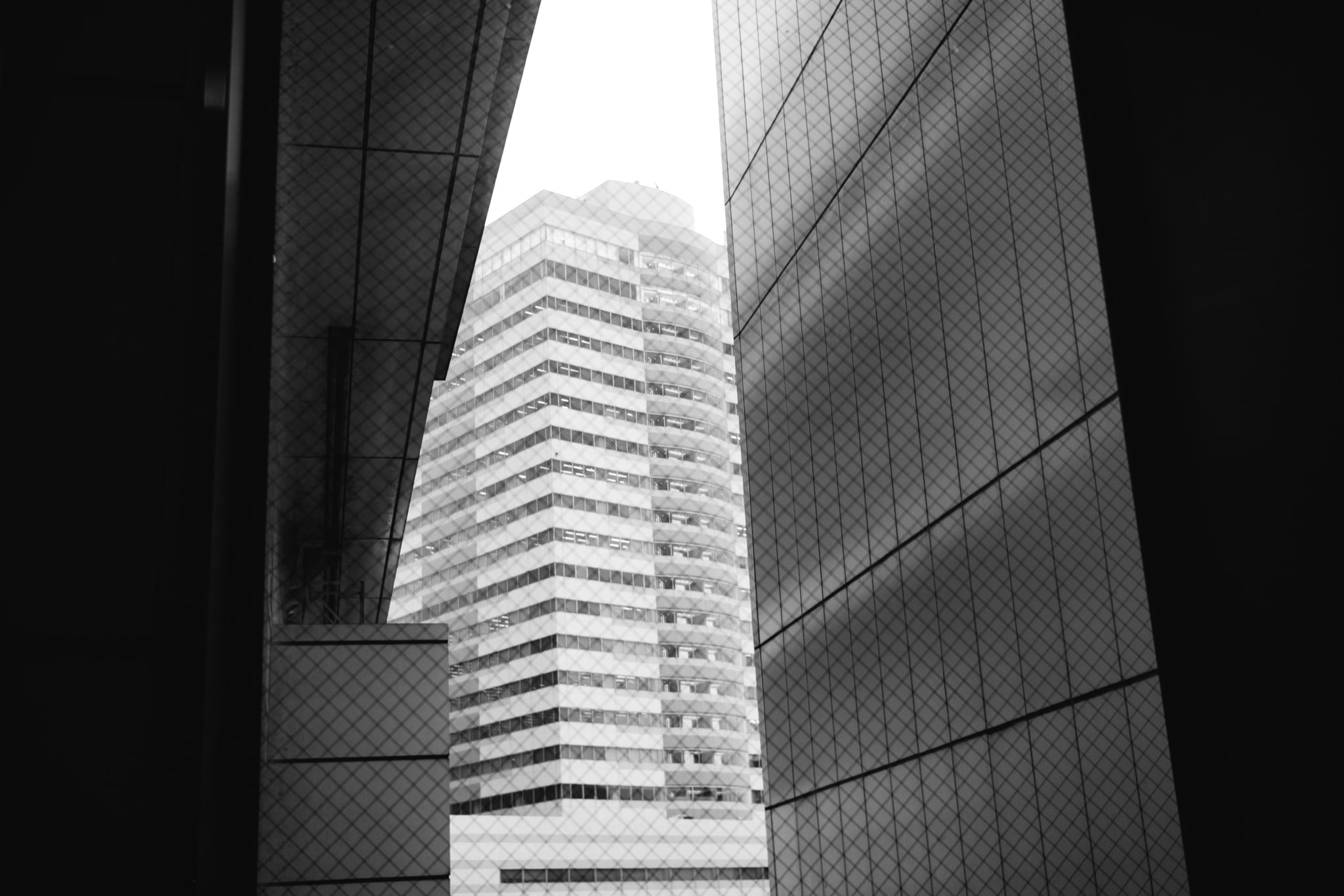 A black and white view of a skyscraper framed by two dark building corners with wire-reinforced glass.