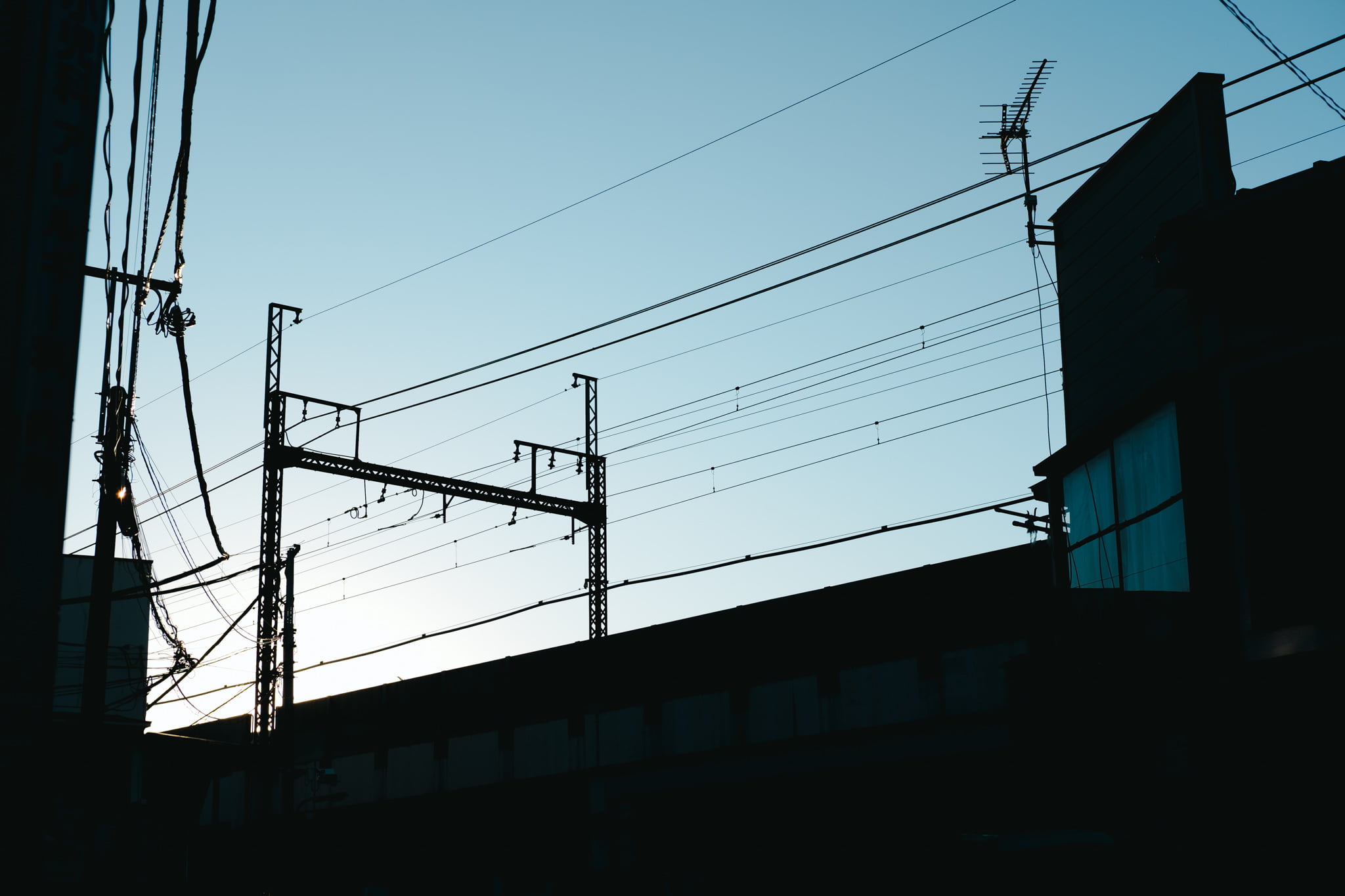 A low-angle view of urban infrastructure silhouetted against a bright, clear blue sky during sunset.