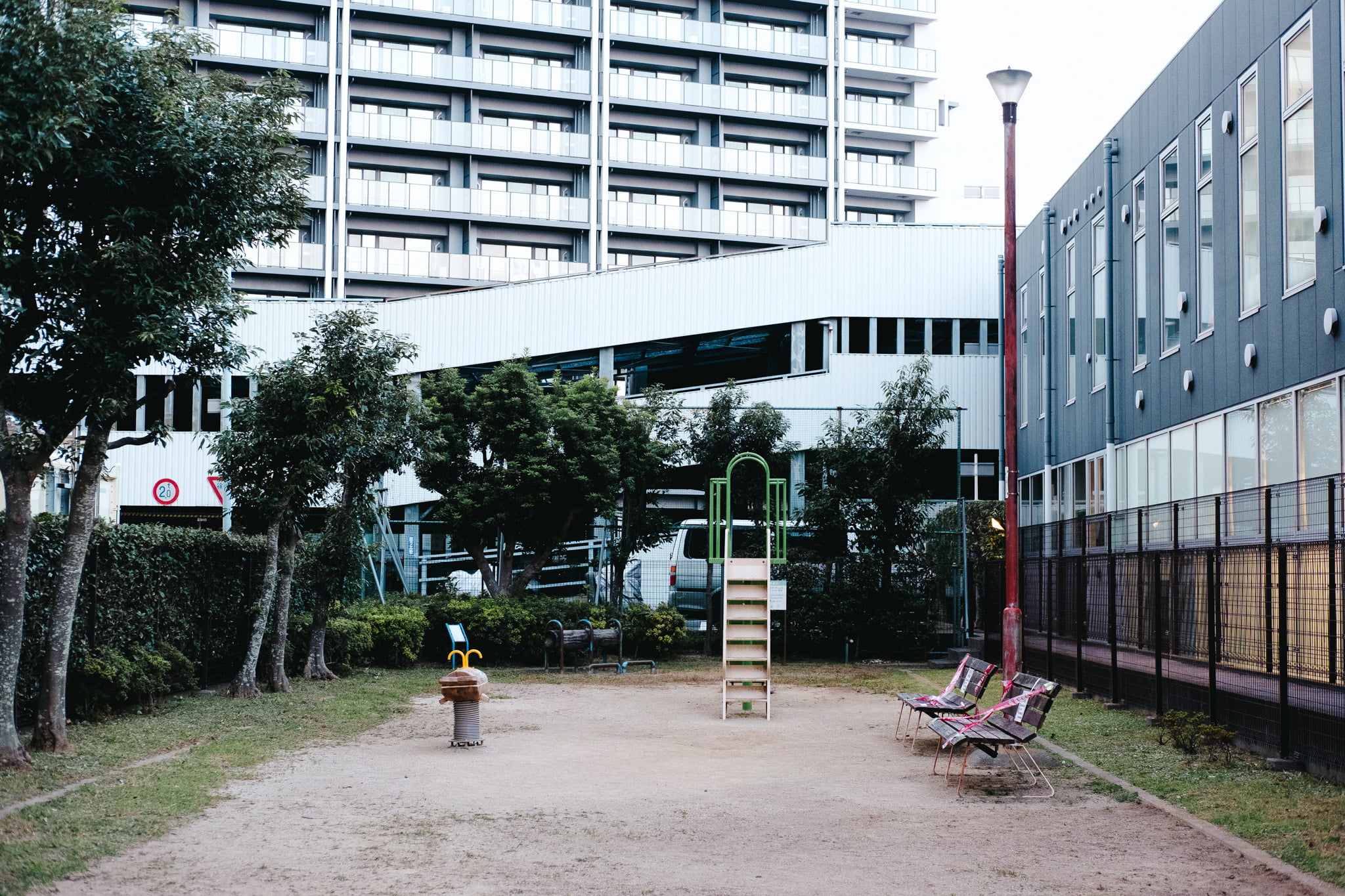 A small urban park featuring a slide, bench, and playground equipment located between modern apartment buildings.