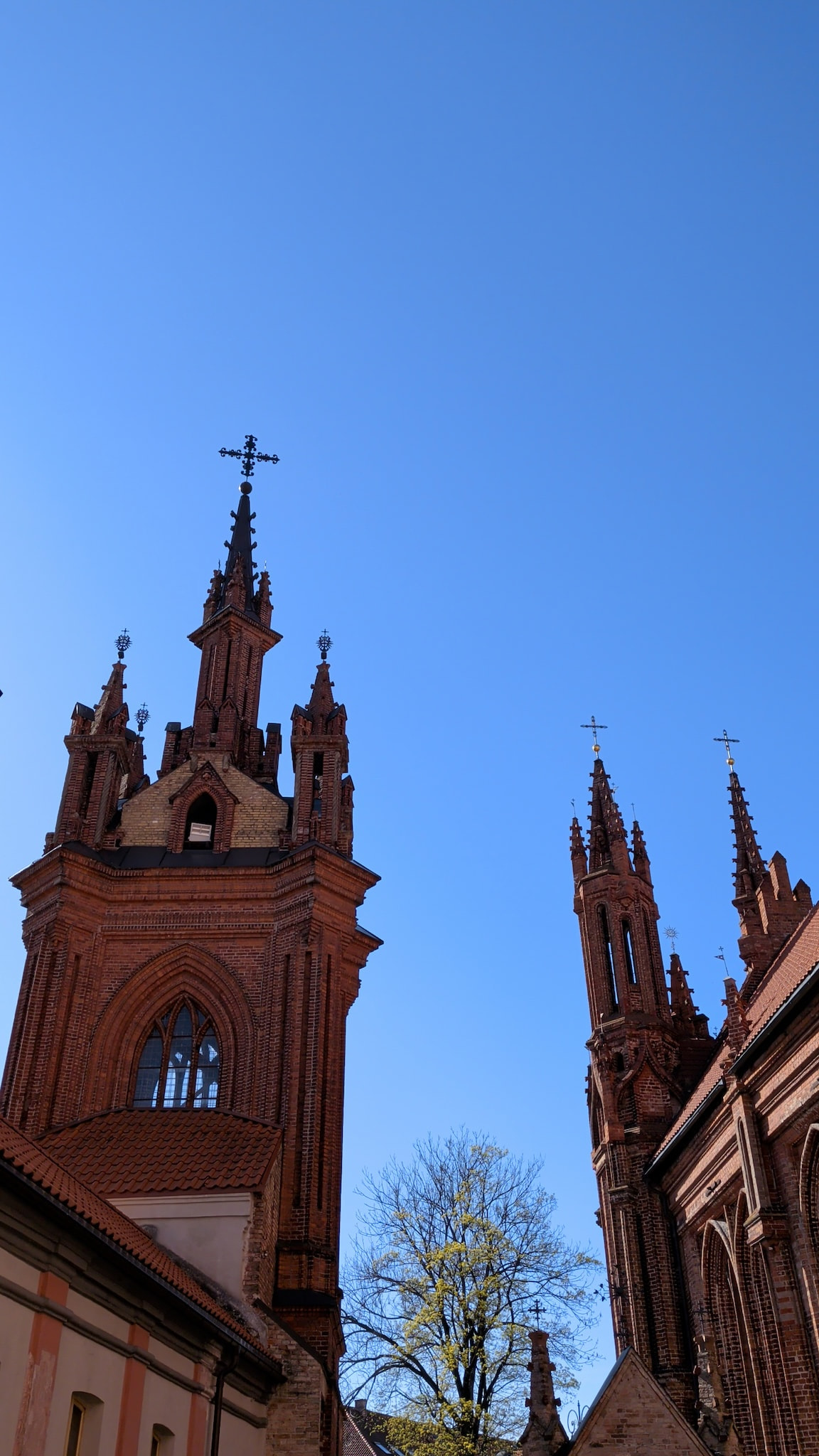 Gothic brick church spires under a clear blue sky.
