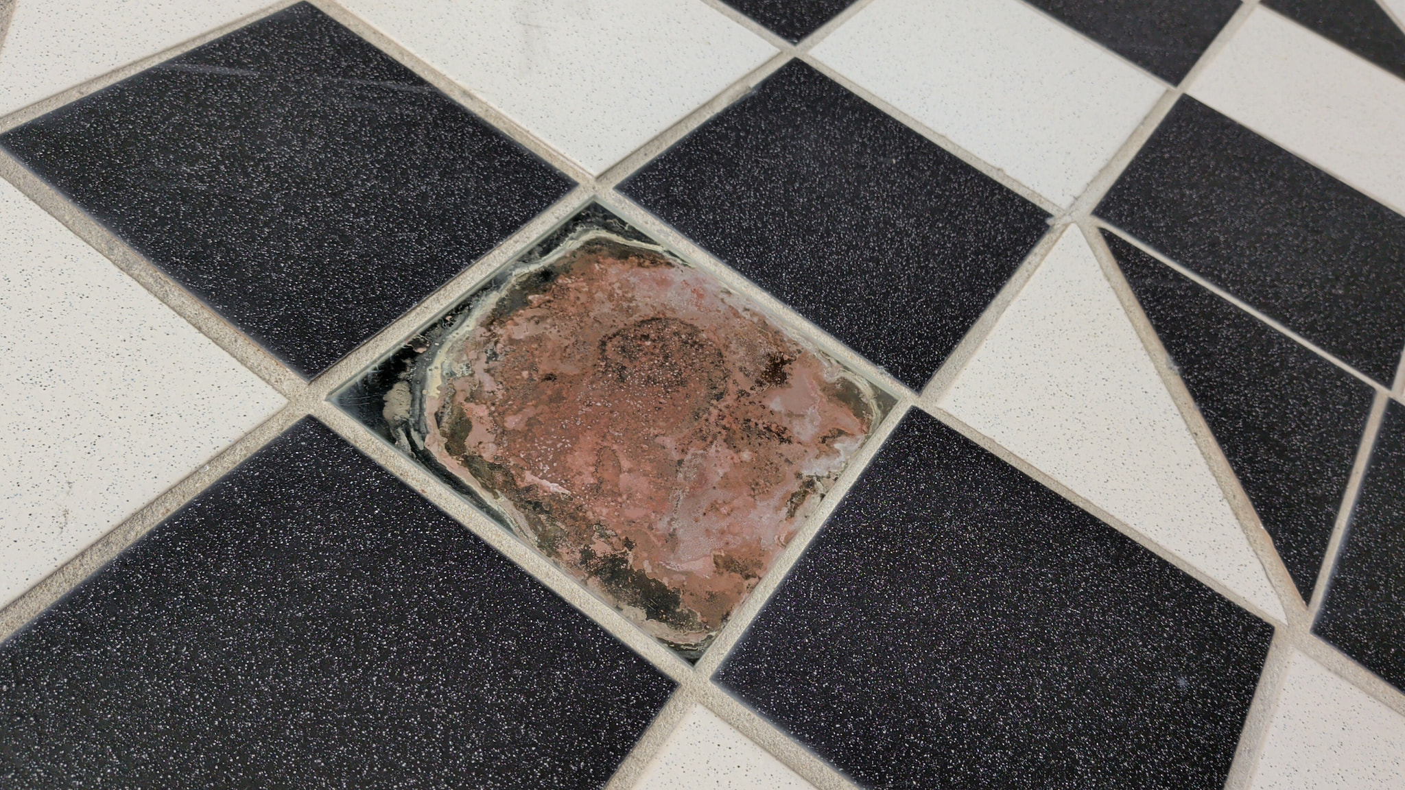 Missing tile in a black and white checkered floor showing subfloor.