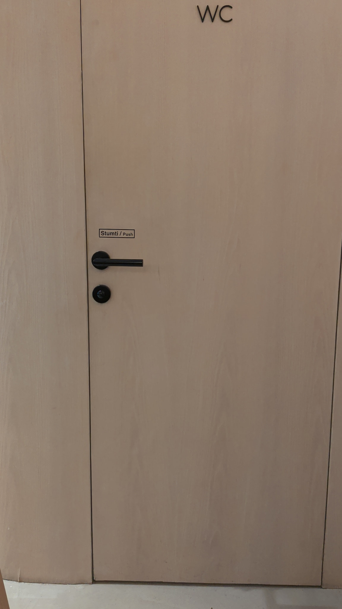 Light wooden door with WC sign and modern black handle