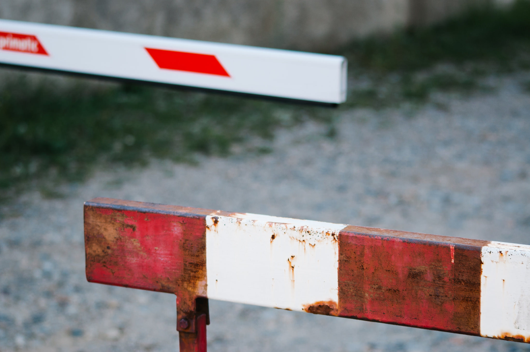 Red and white barrier gate lowered across gravel road