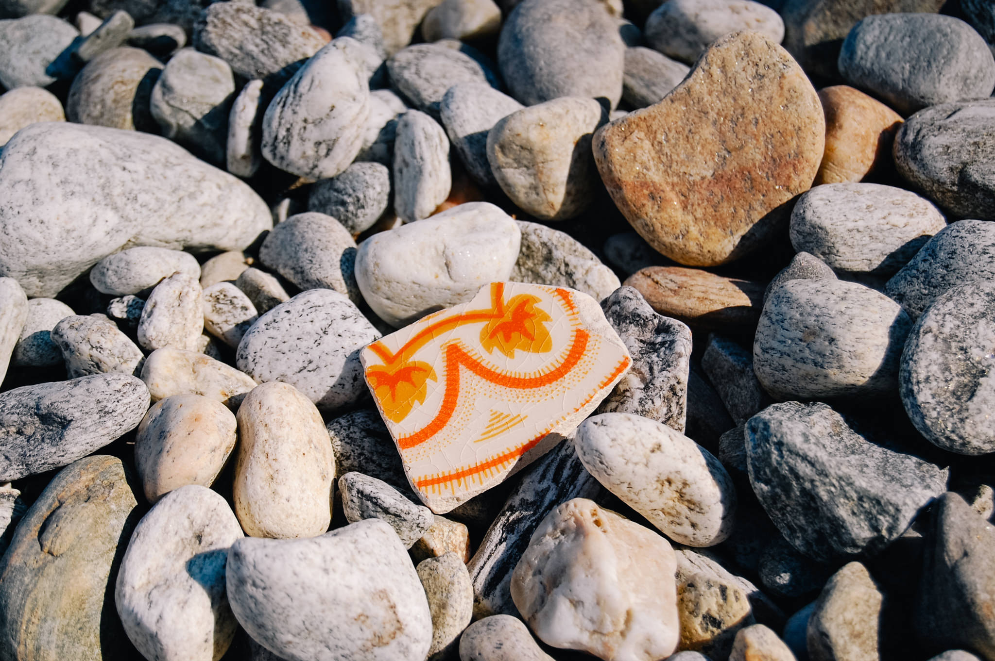 Ceramic shard with orange leaf pattern resting on pebble beach